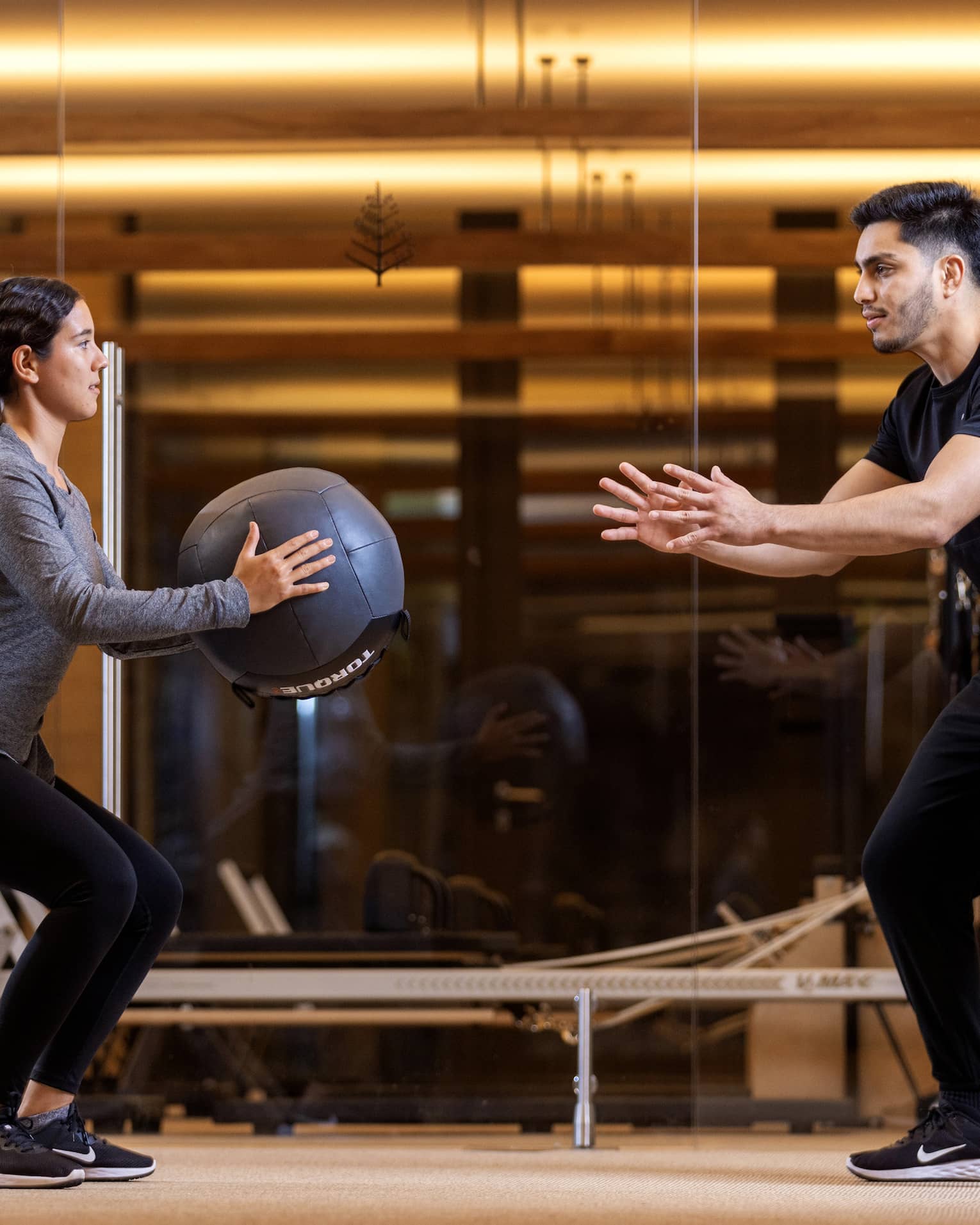 Two people exercise with an exercise ball in an indoor fitness centre setting.
