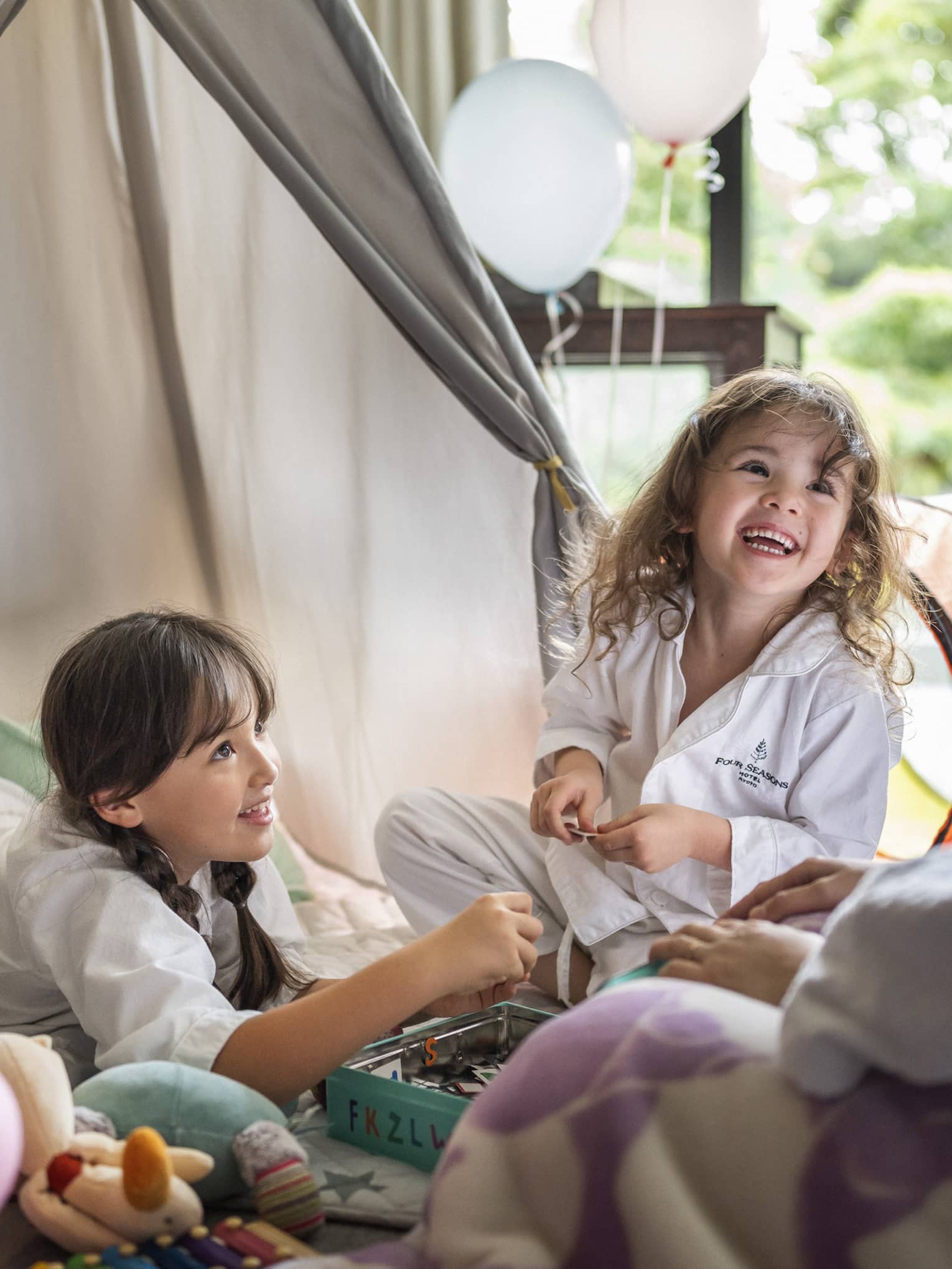 Two children in Four Seasons pajamas, smiling and playing together in a cozy indoor tent setup
