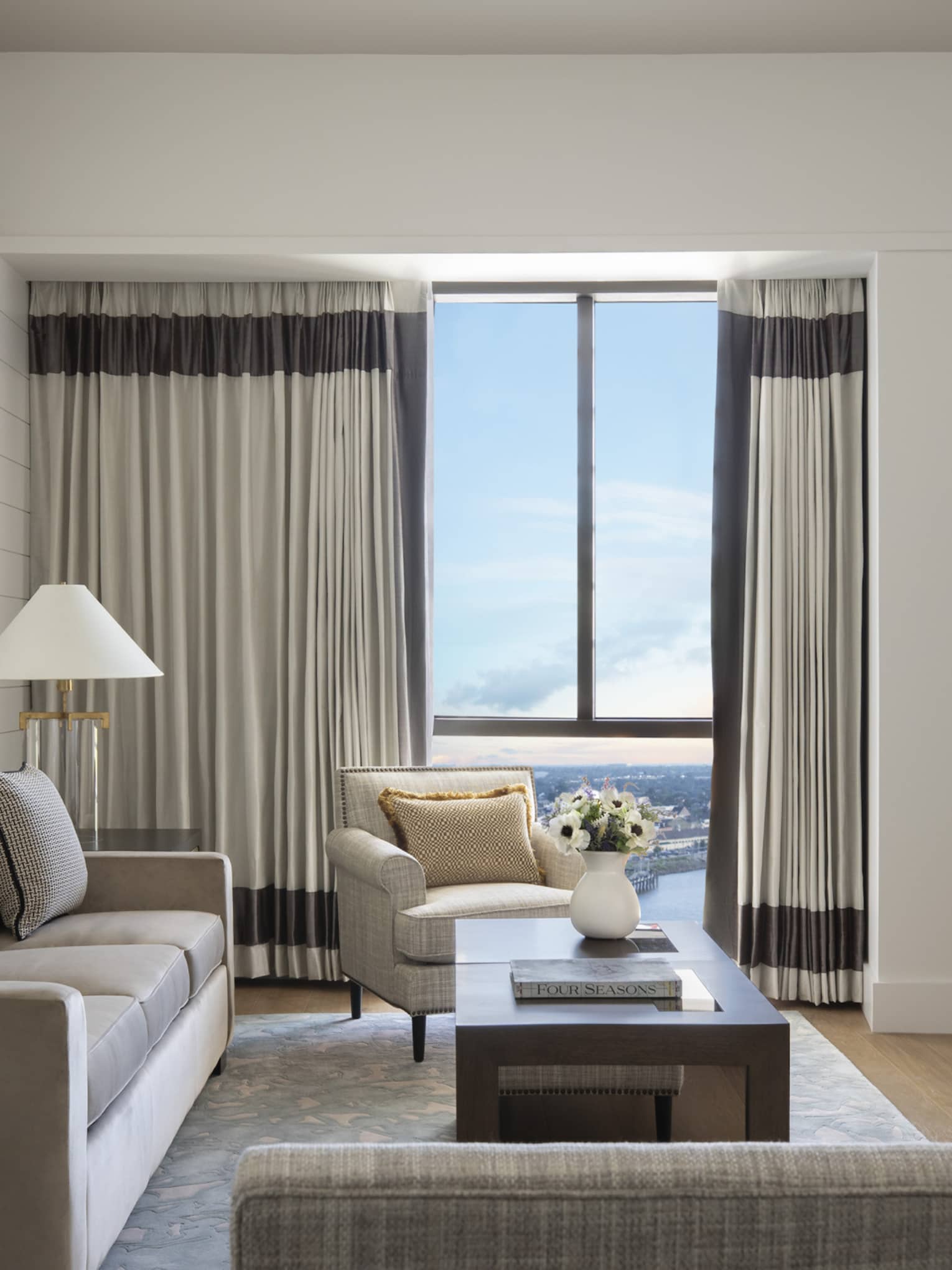 Living room with grey sofa, arm chair, TV, glass table lamps and windows