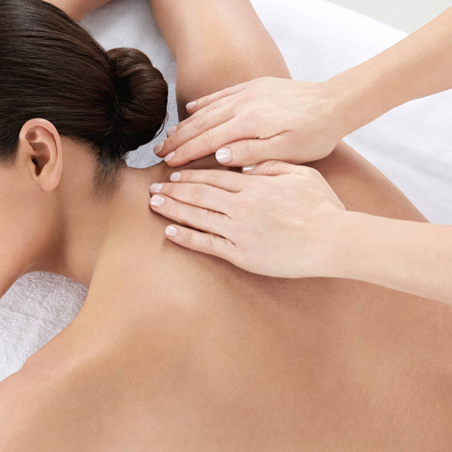 Woman smiles, lies on massage table as hands massage bare shoulders