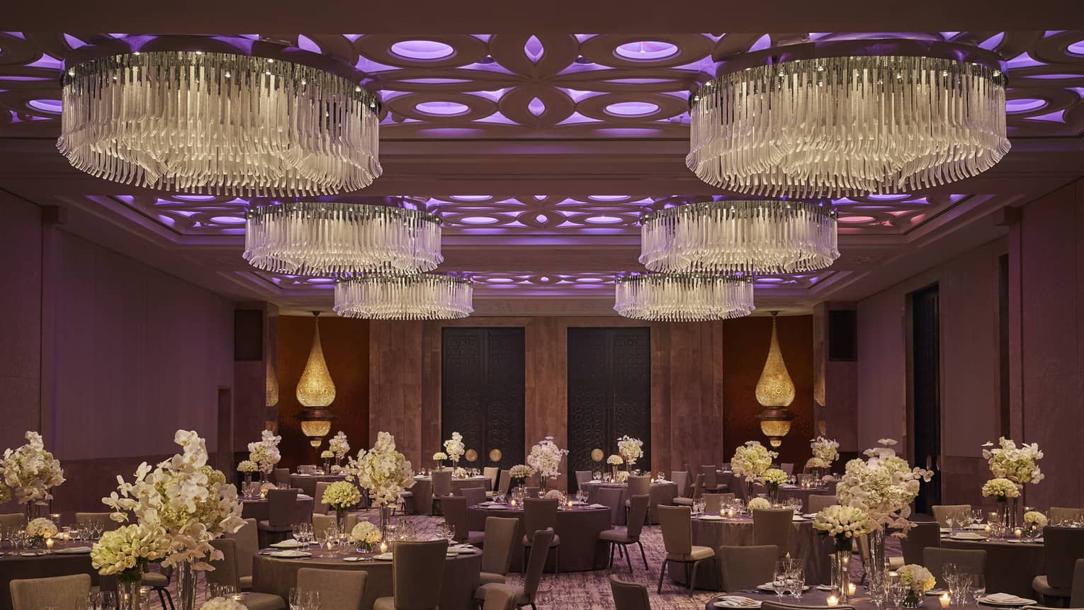 Round banquet dining tables in ballroom with round chandeliers, purple lights on ceiling
