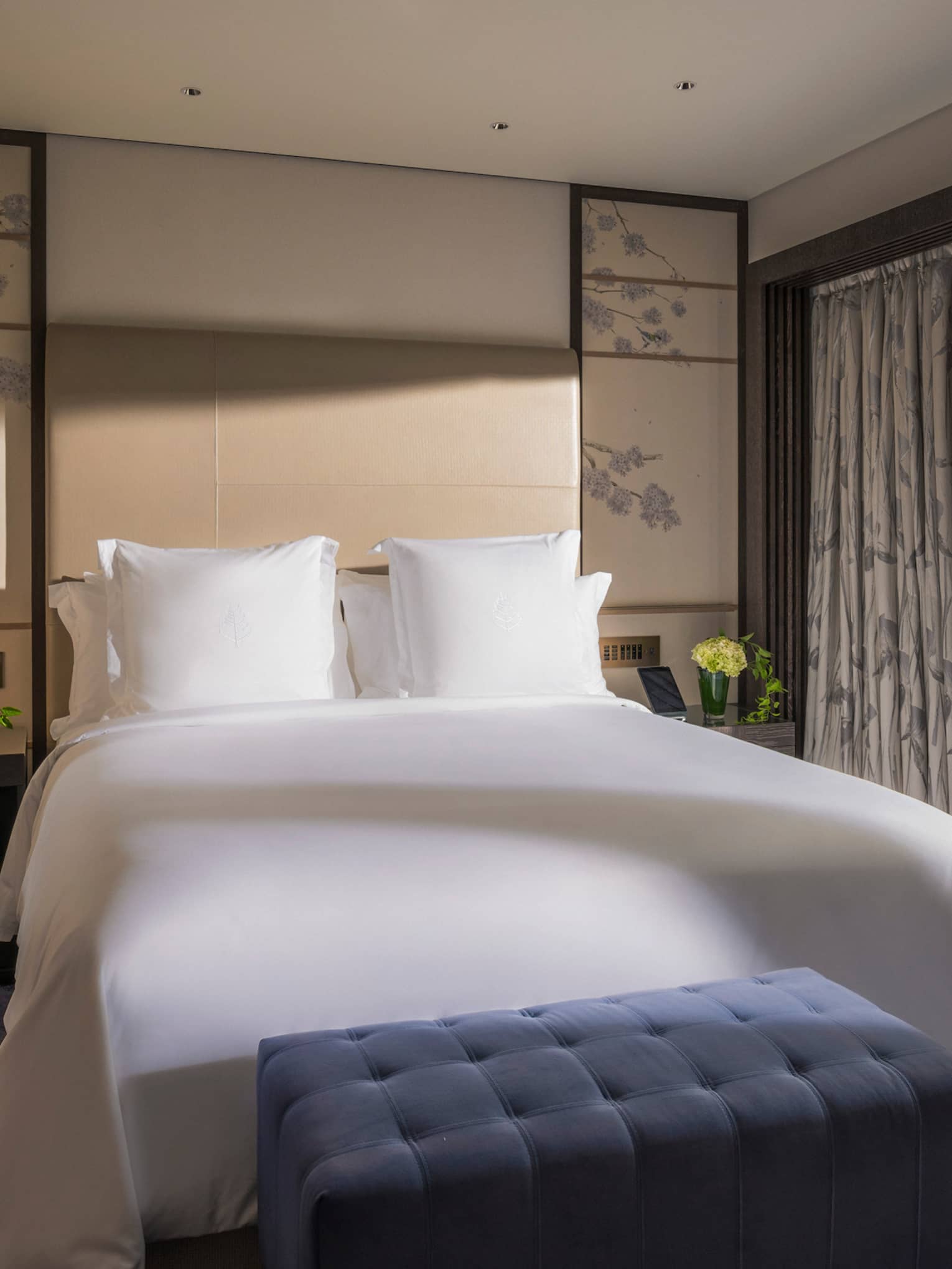 Bright bedroom with a king-size bed, a blue tufted bench and sliding glass doors opening to a private terrace with garden view