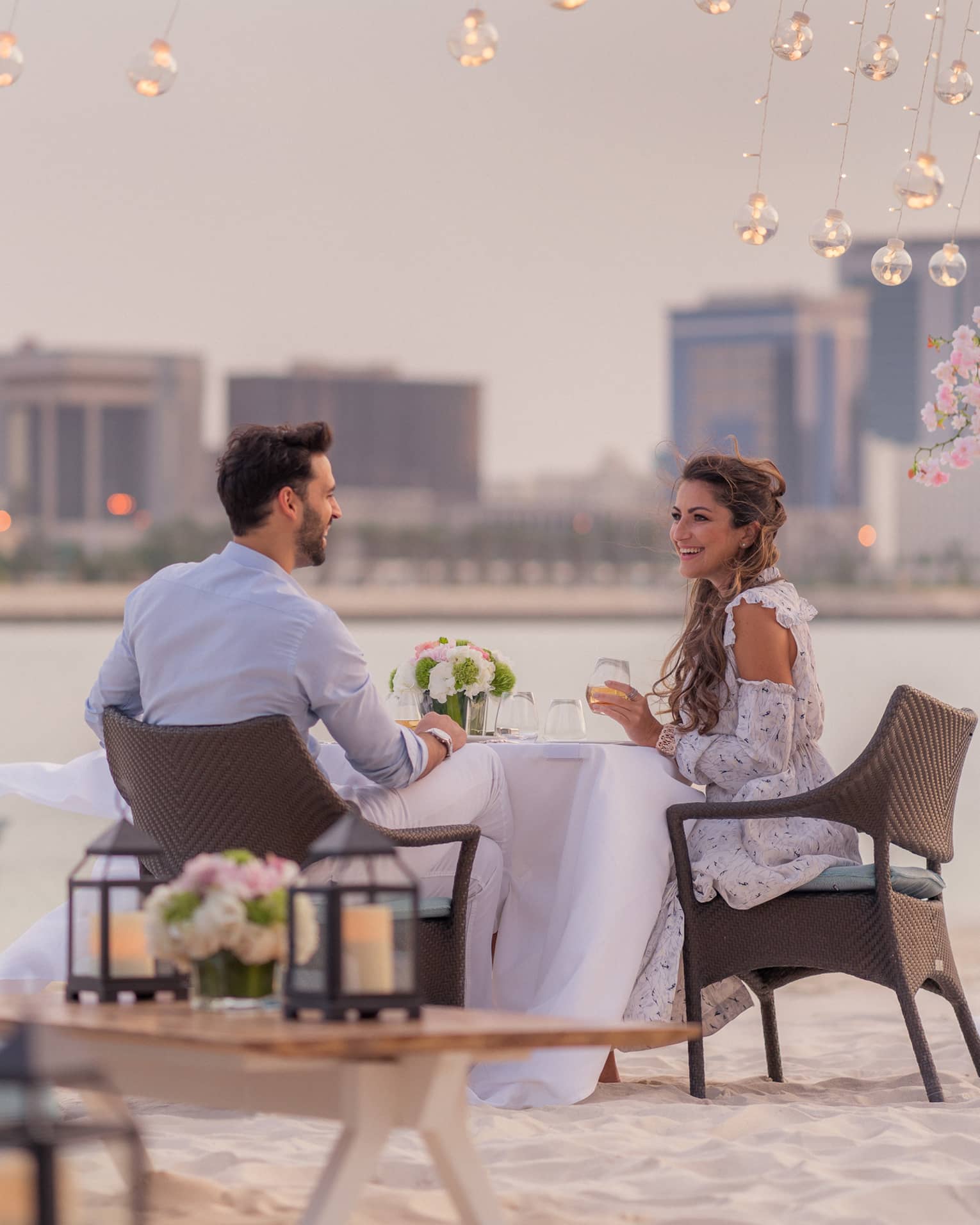 A man and woman enjoy a romantic dinner outside by the water overlooking the city