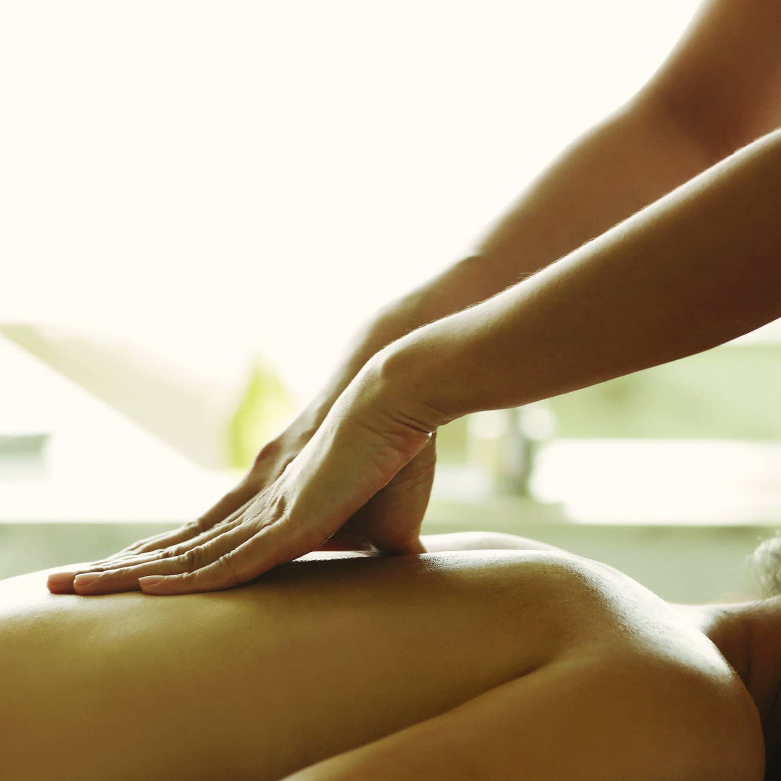 Masseuse reaches over, massages woman's bare back as she lies on spa table