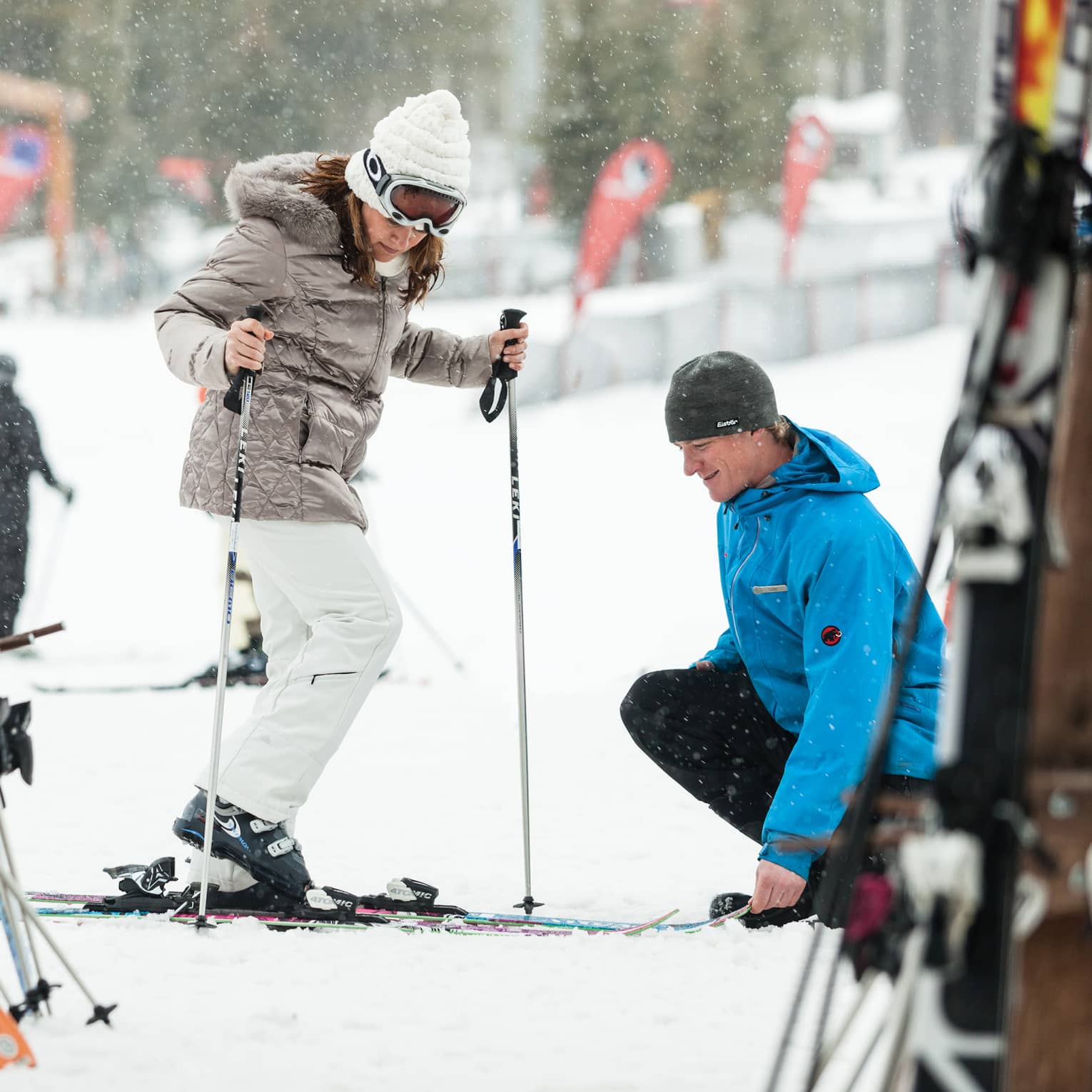 Ski concierge kneels down by woman trying on skis in front of rack