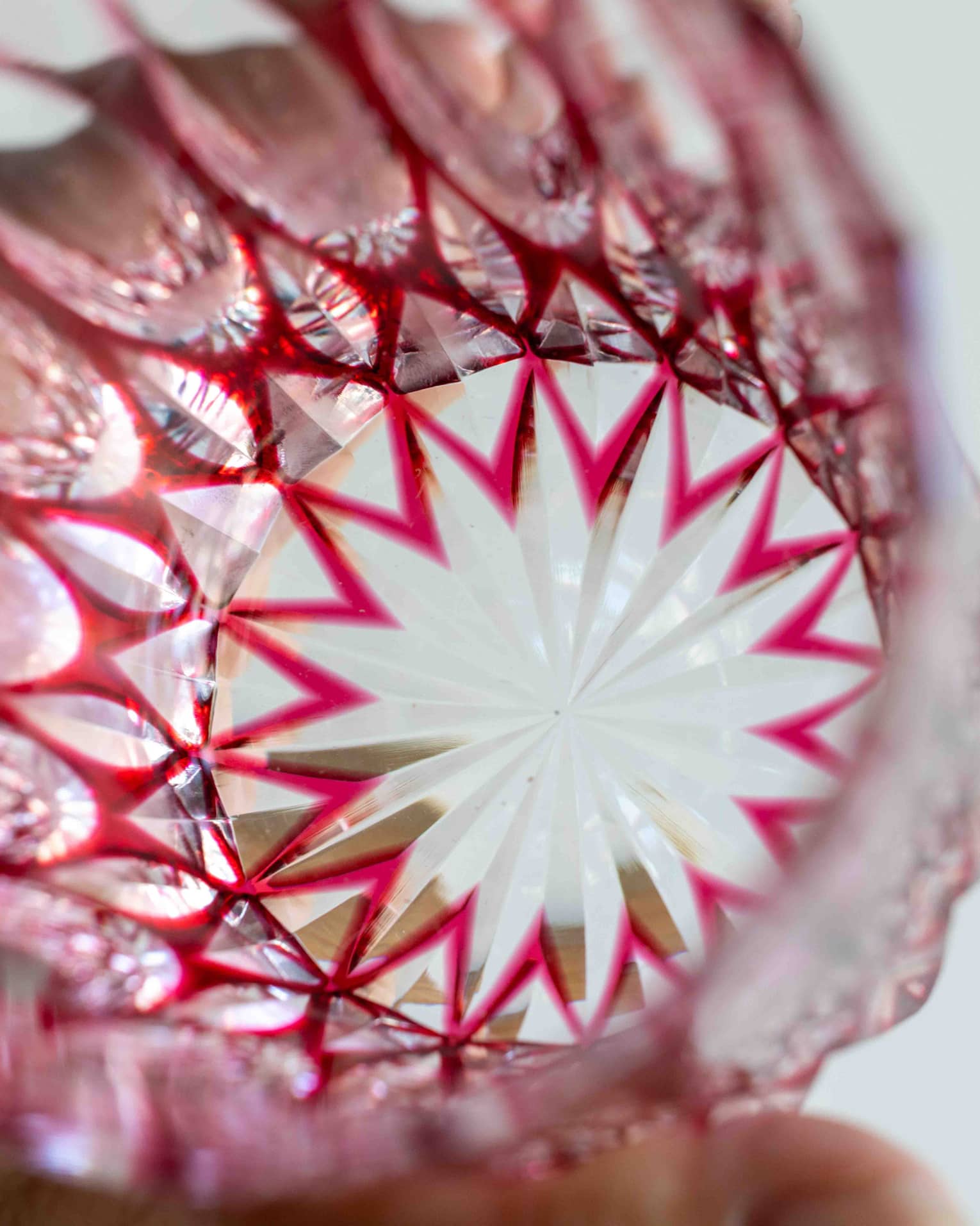 Extreme close-up inside a bright-red cut glass tumbler with a starburst base and intricate geometric patterns on the sides.