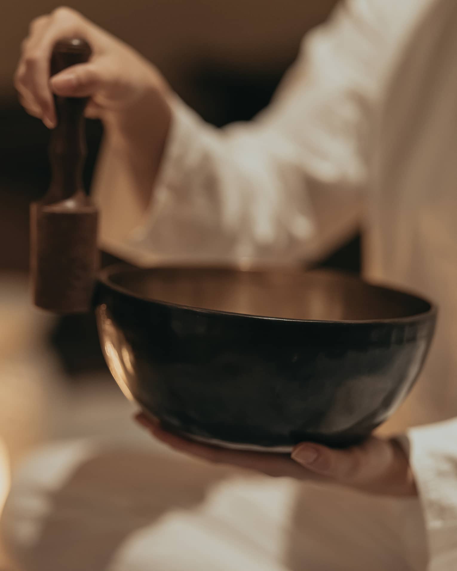 Close-up of an instructor rubbing a mallet against the edge of a sound bowl in a dimly lit room surround by burning candles.