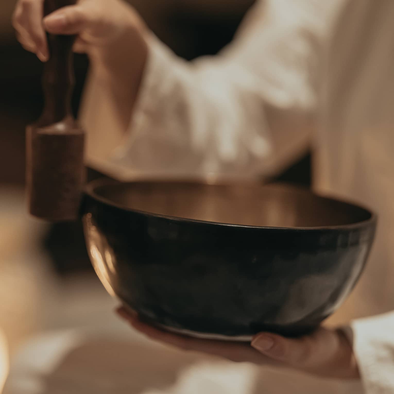 Close-up of an instructor rubbing a mallet against the edge of a sound bowl in a dimly lit room surround by burning candles.