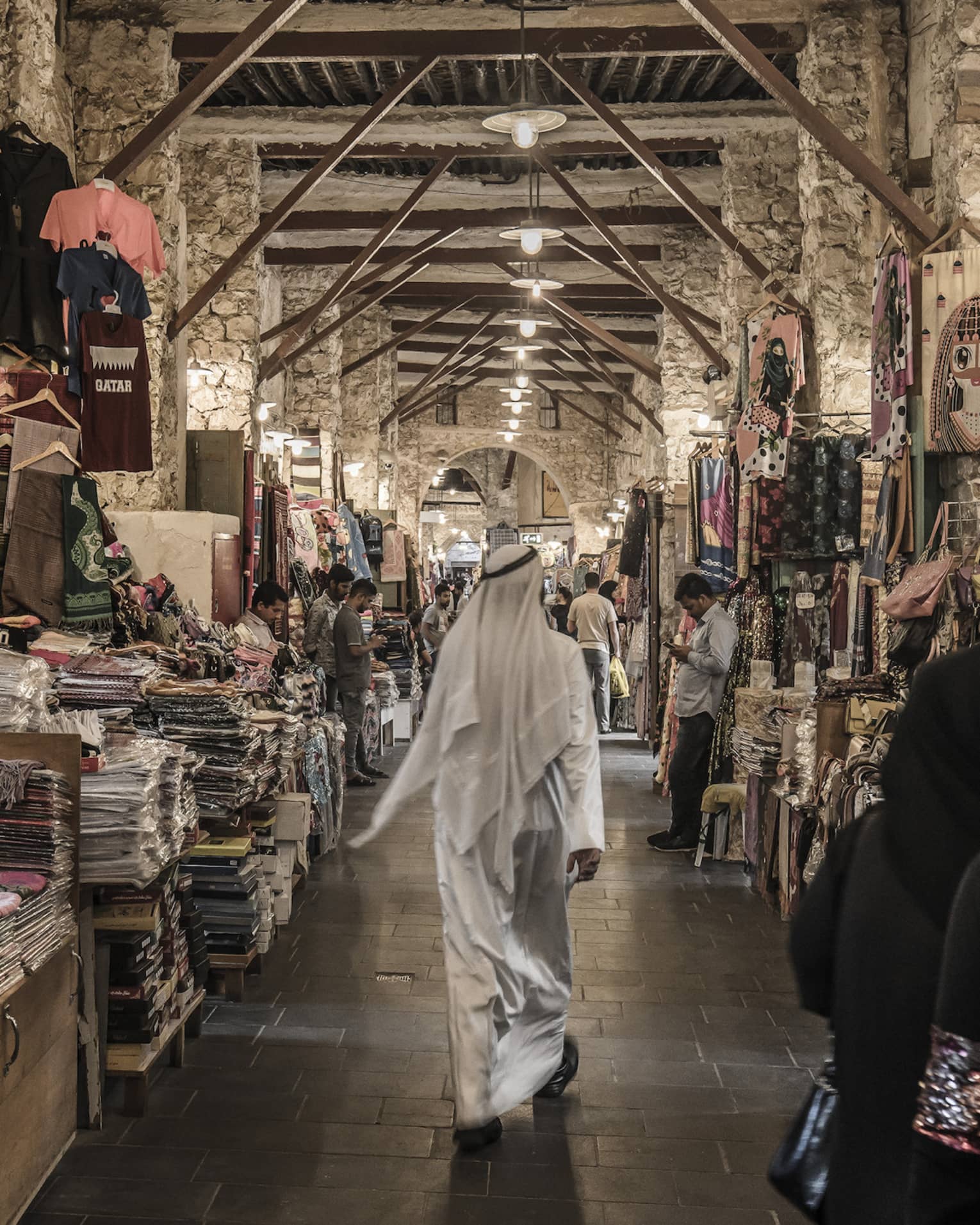 People walk past tables with textiles, clothes in indoor market