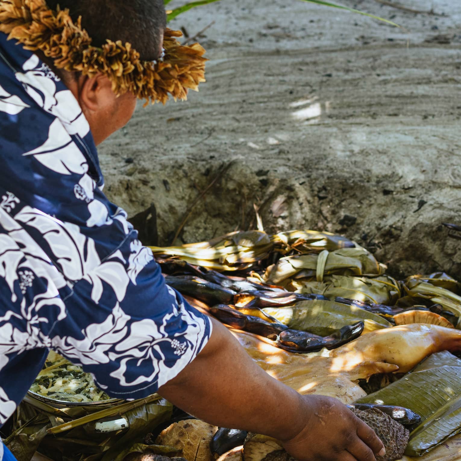 A chef places meat in a Tahitian oven: a hole dug into the sand filled with hot stones and palm leaves.