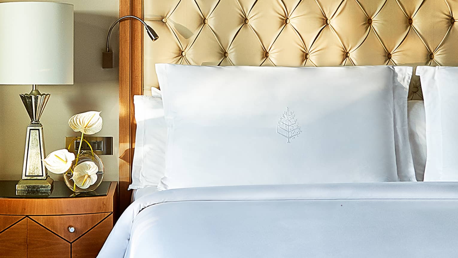 Royal Suite close-up of white pillows and tall leather headboard, wooden side table with lamp and white orchids