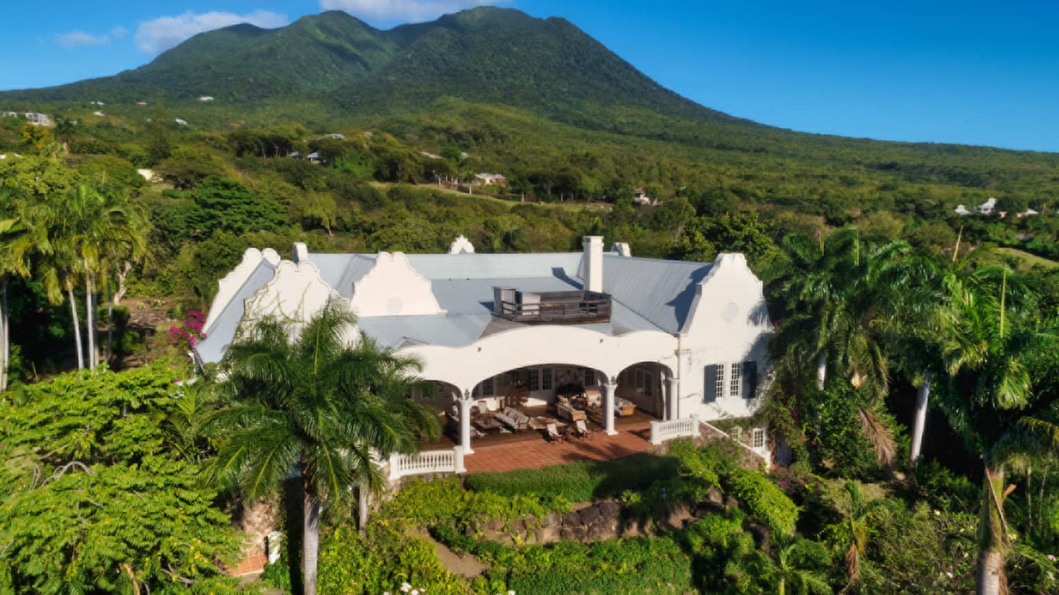Exterior of a private villa at Four Seasons Resort and Residences Nevis, with lush gardens and Nevis Peak in the background