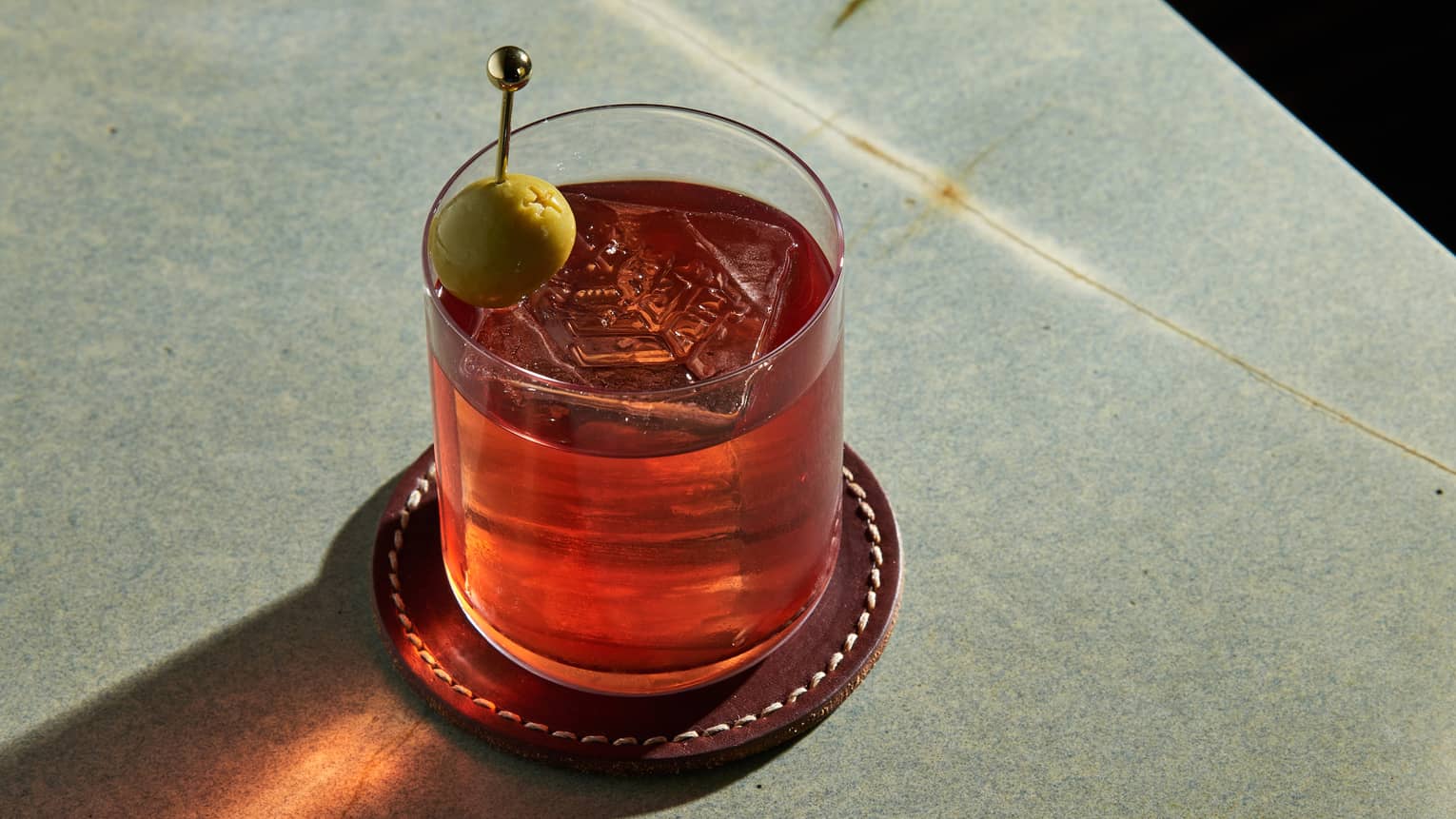Red-coloured cocktail in a rocks glass garnished with a green olive