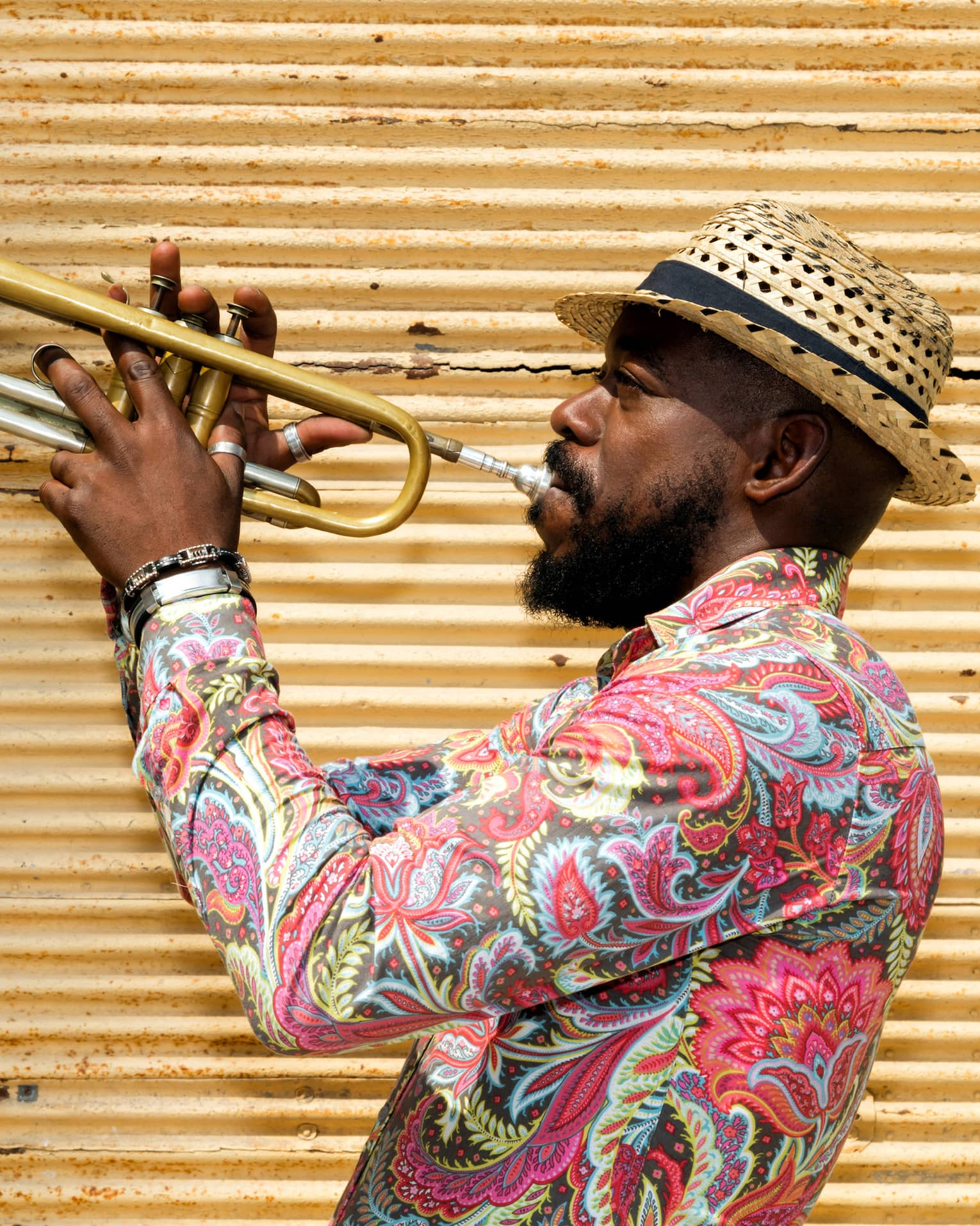A man in a hat and colourful shirt playing a trumpet.