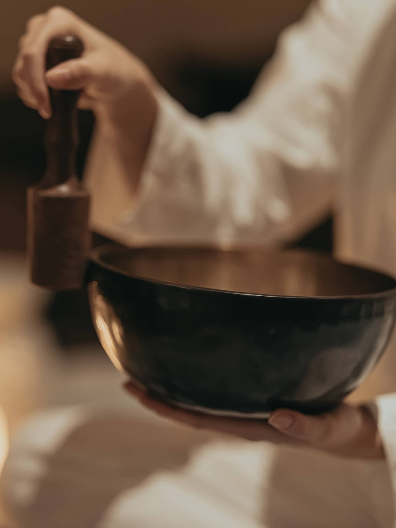 Close-up of an instructor rubbing a mallet against the edge of a sound bowl in a dimly lit room surround by burning candles.
