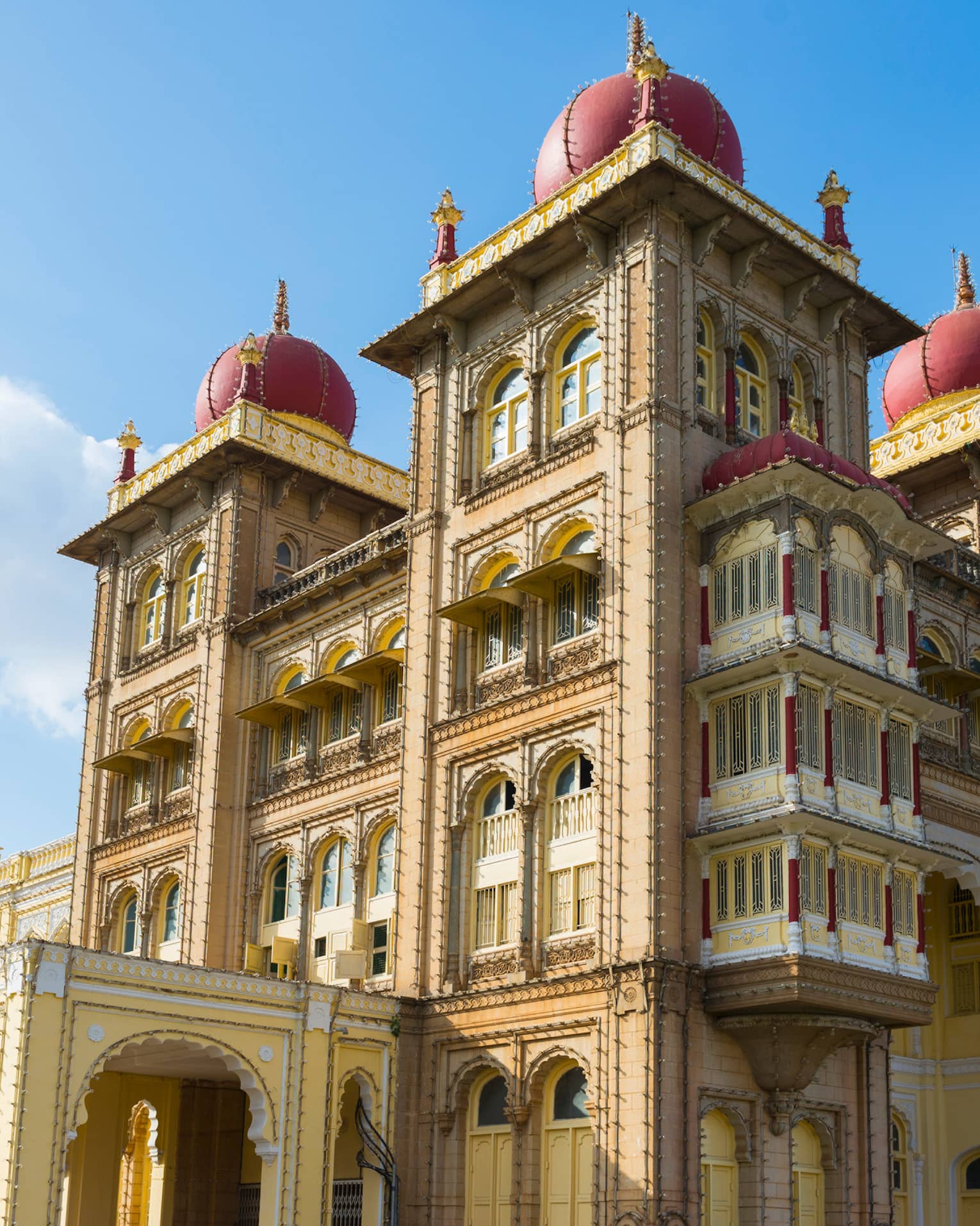 Sprawling palace with arched windows, dome-topped towers and an ornate design, its golden hue contrasted against a sunny sky.