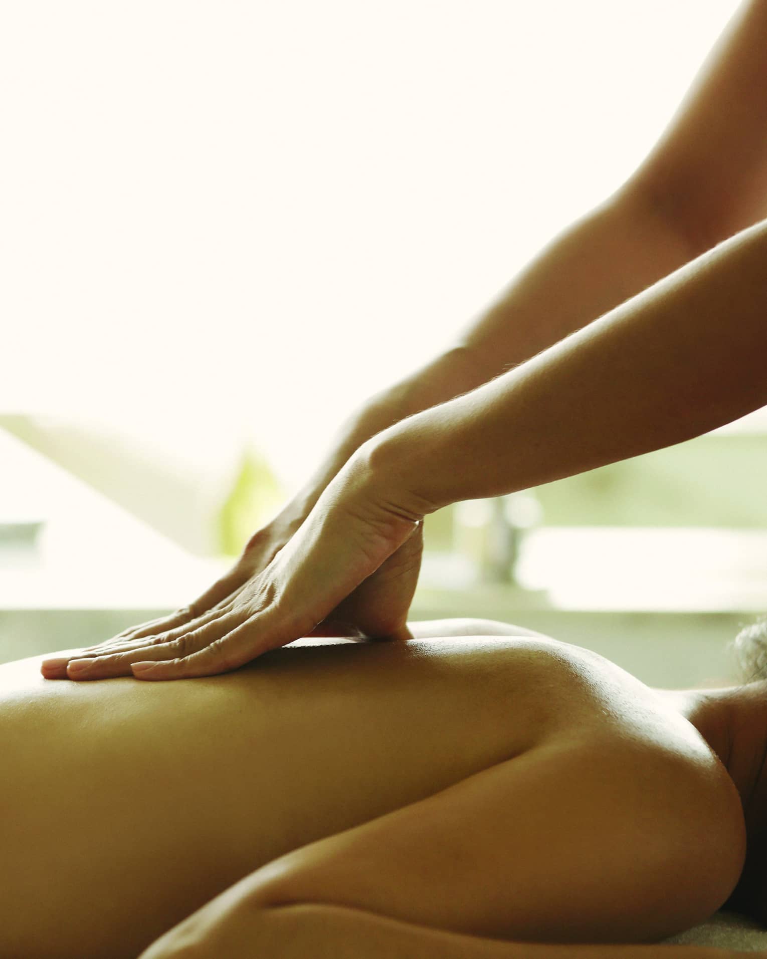 Masseuse reaches over, massages woman's bare back as she lies on spa table