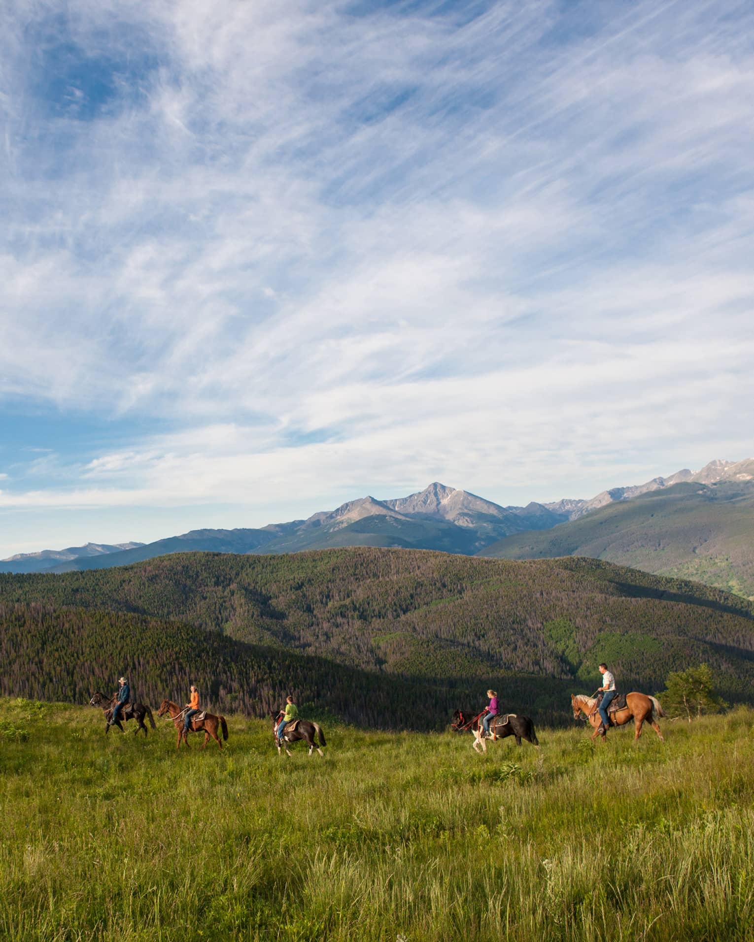 A group of people on horseback riding along grass and hills.