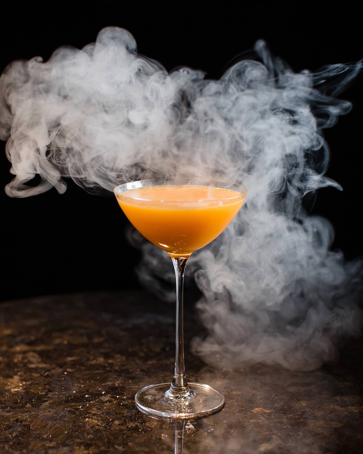 Orange cocktail in martini glass surrounded by smoke