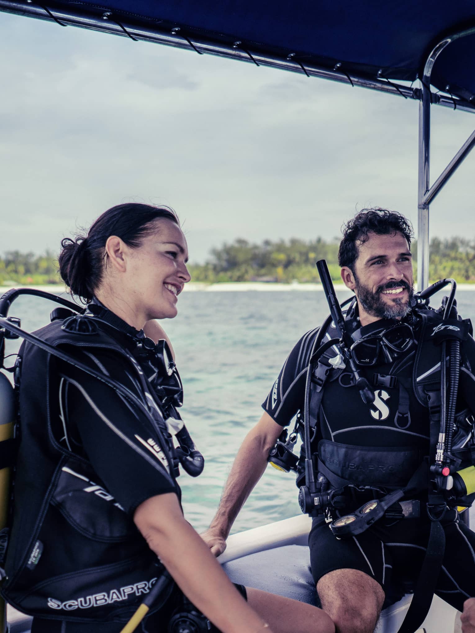 Three people in SCUBA gear with tanks on boat in ocean smiling and talking