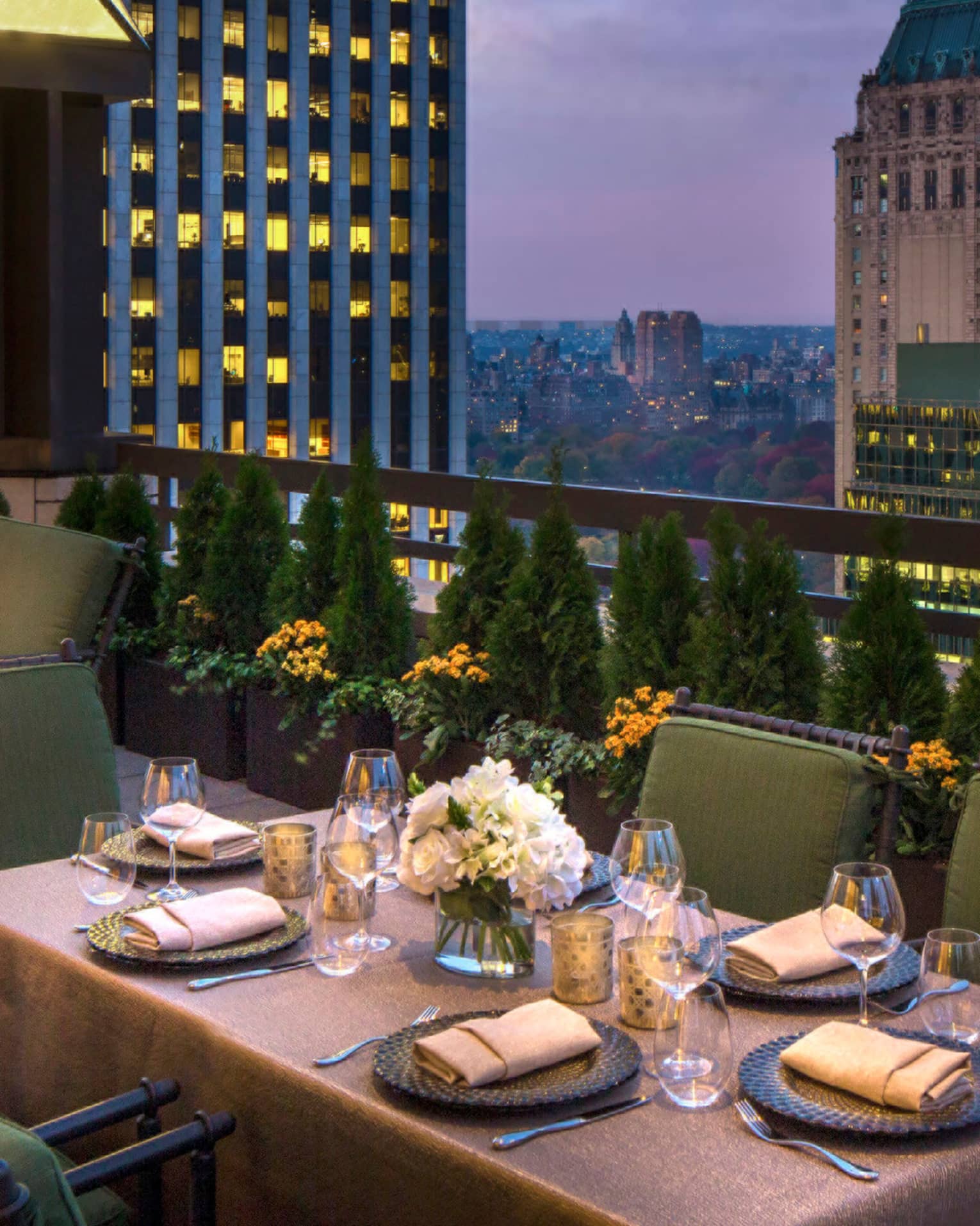 Private patio dining table with plush green cushions on chairs on rooftop terrace, city views at dusk