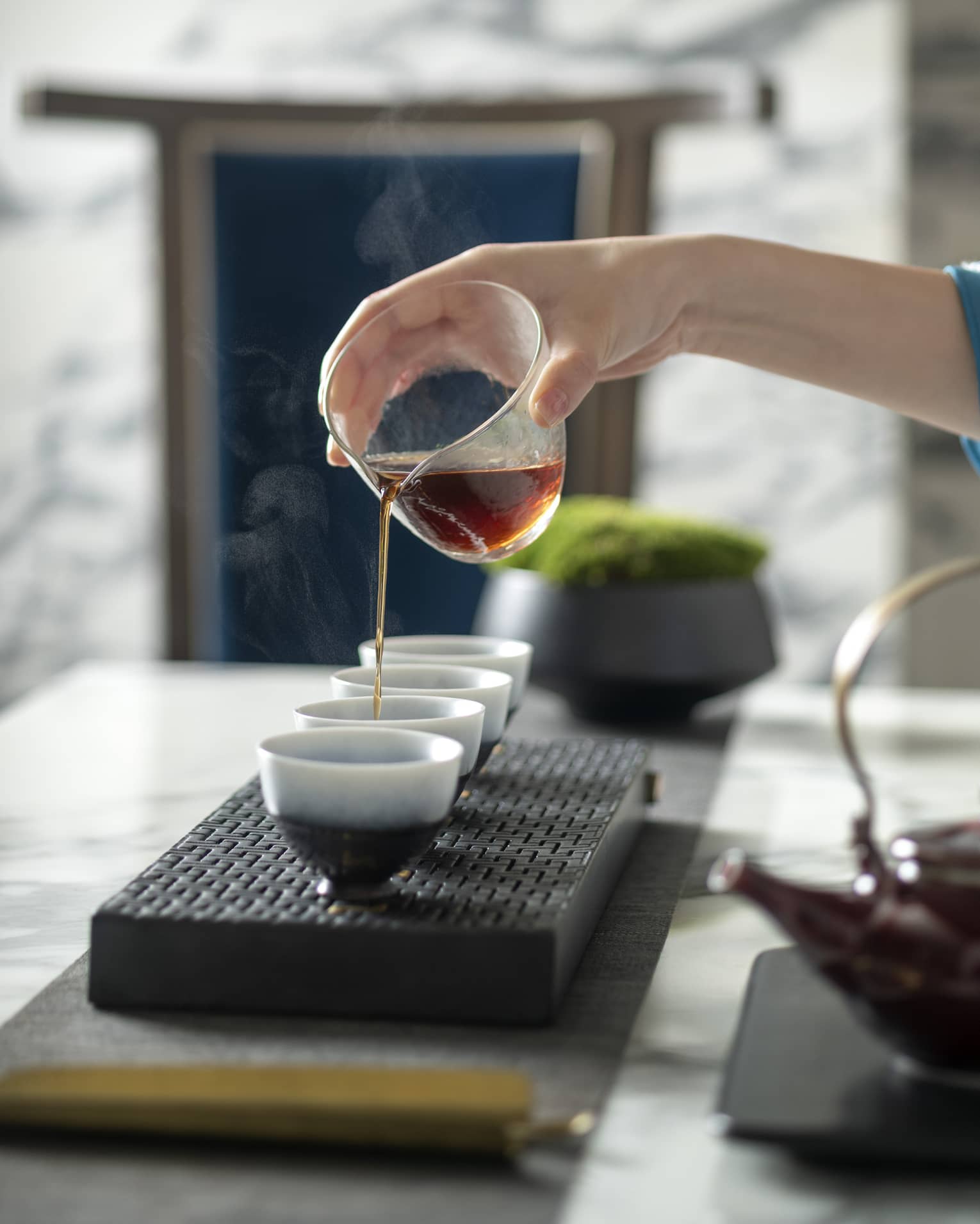 Woman's hand pours tea into mugs for traditional tea ceremony