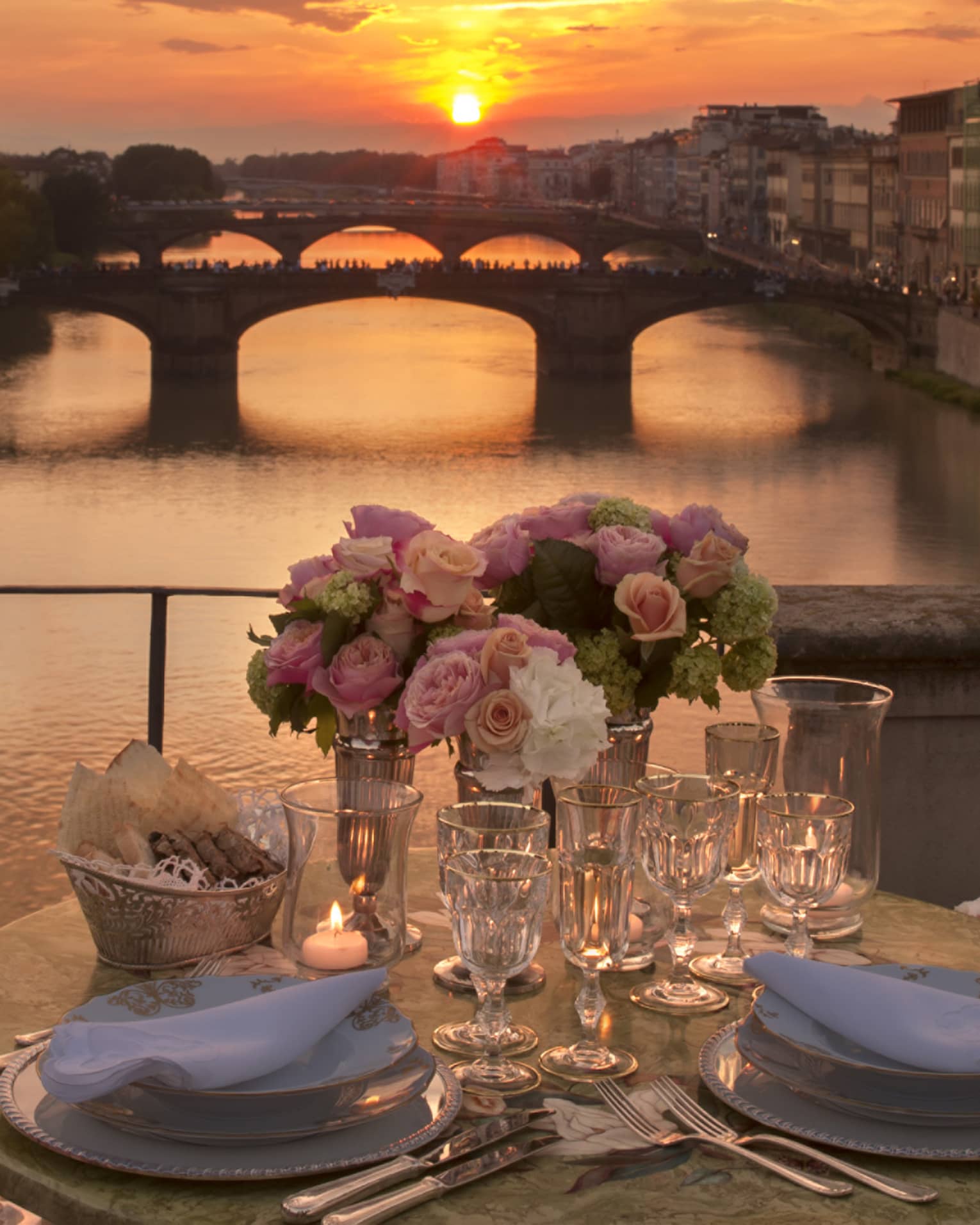 Pink roses in vases on formal dining table on bridge overlooking canal, sunset