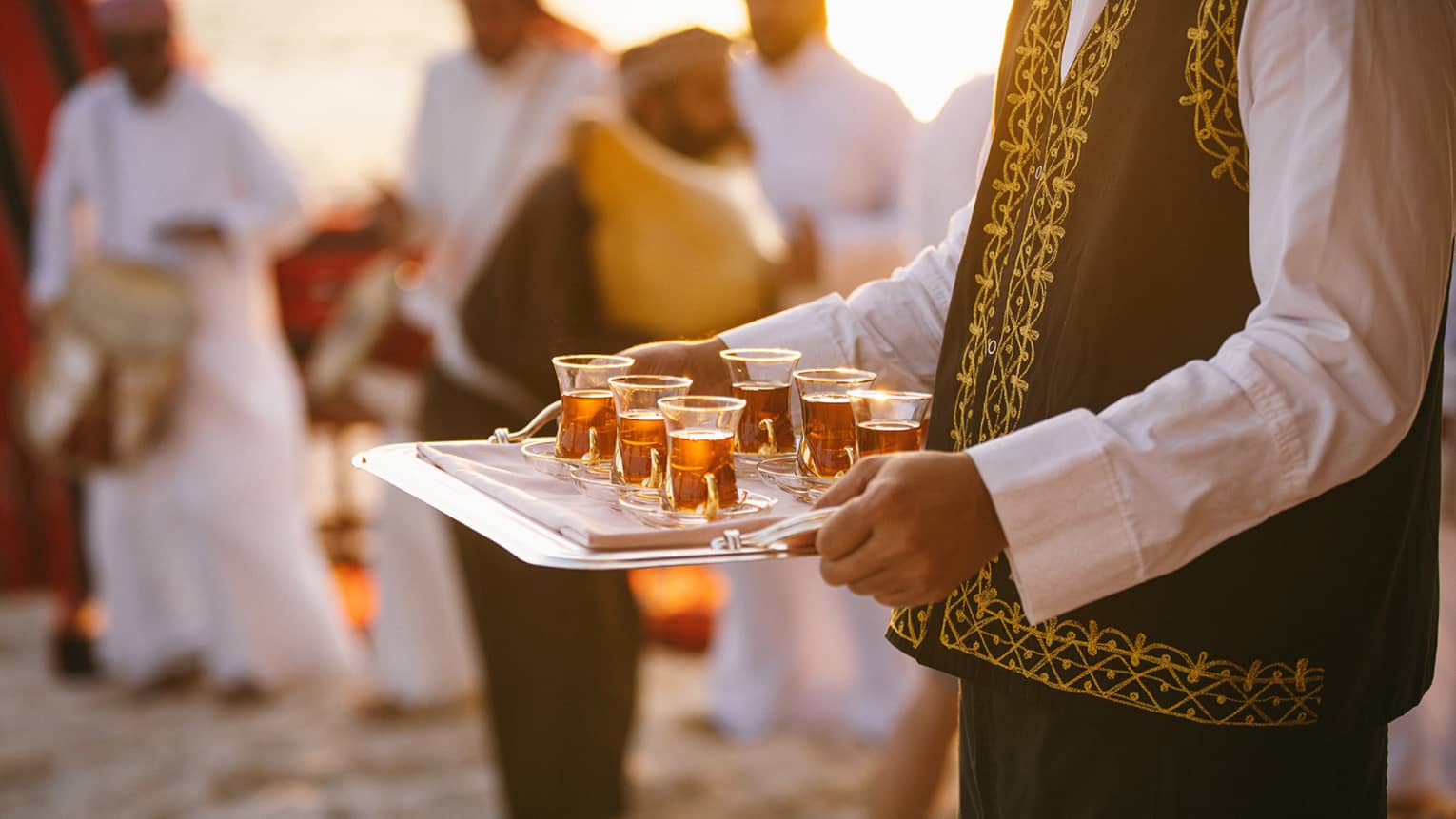Staff carries tray with tea along sand beach as band plays