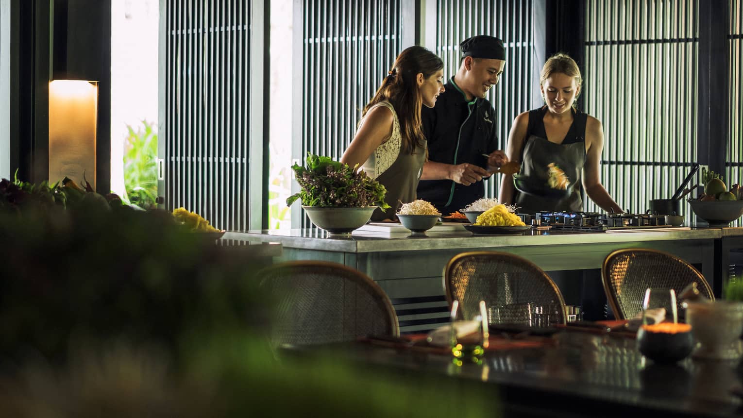Chef, two women look at pan on kitchen range at Hoi An Cooking Academy 