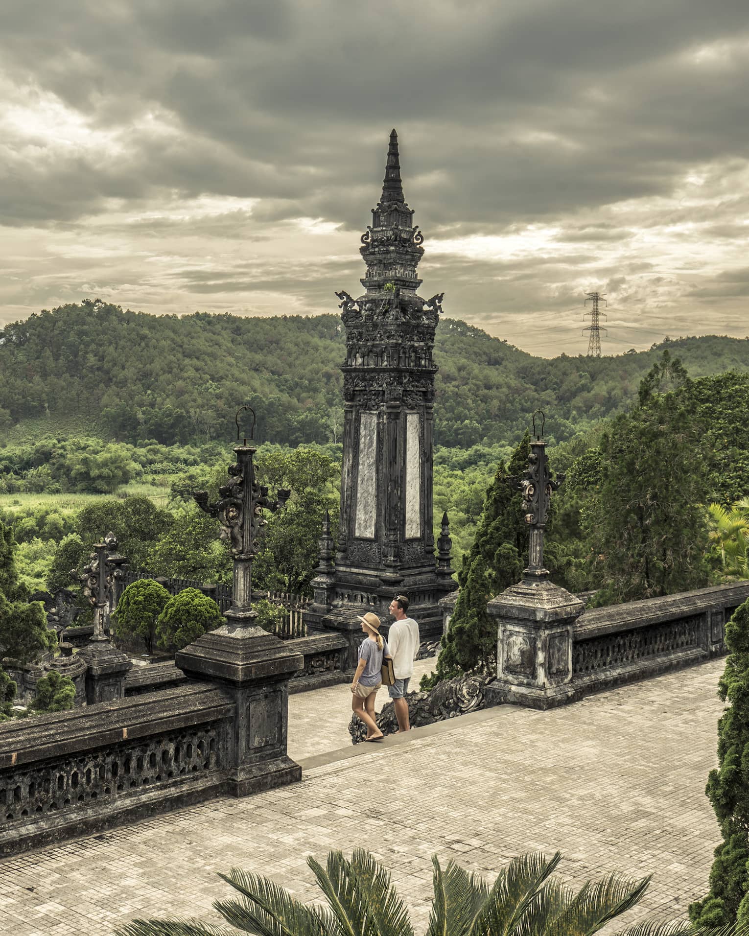 Man and woman walk down steps of historic Imperial City of Hue with stone towers, rolling hills