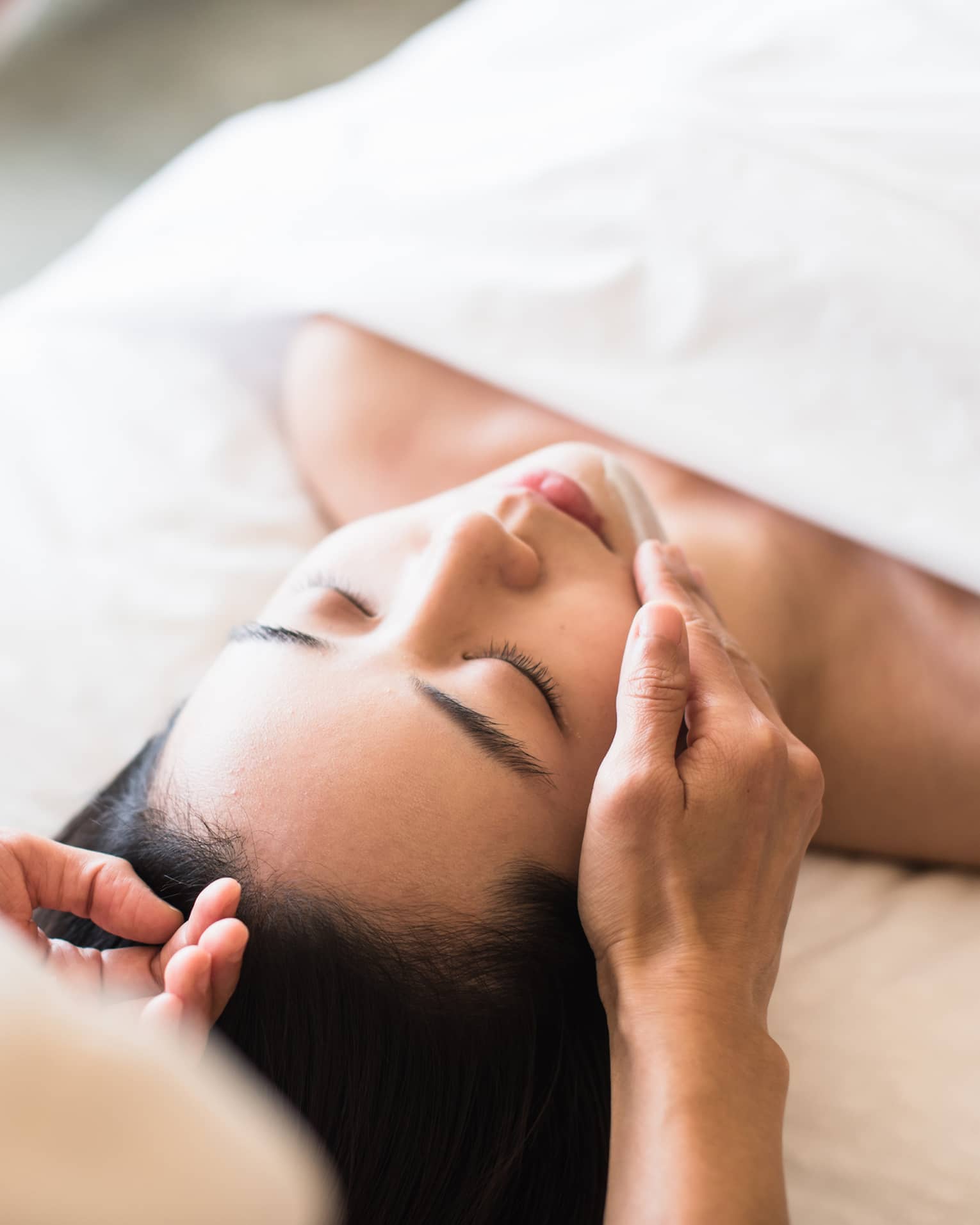 A guest receiving a soothing facial at a spa, lying on a massage table, surrounded by calming décor and soft lighting.