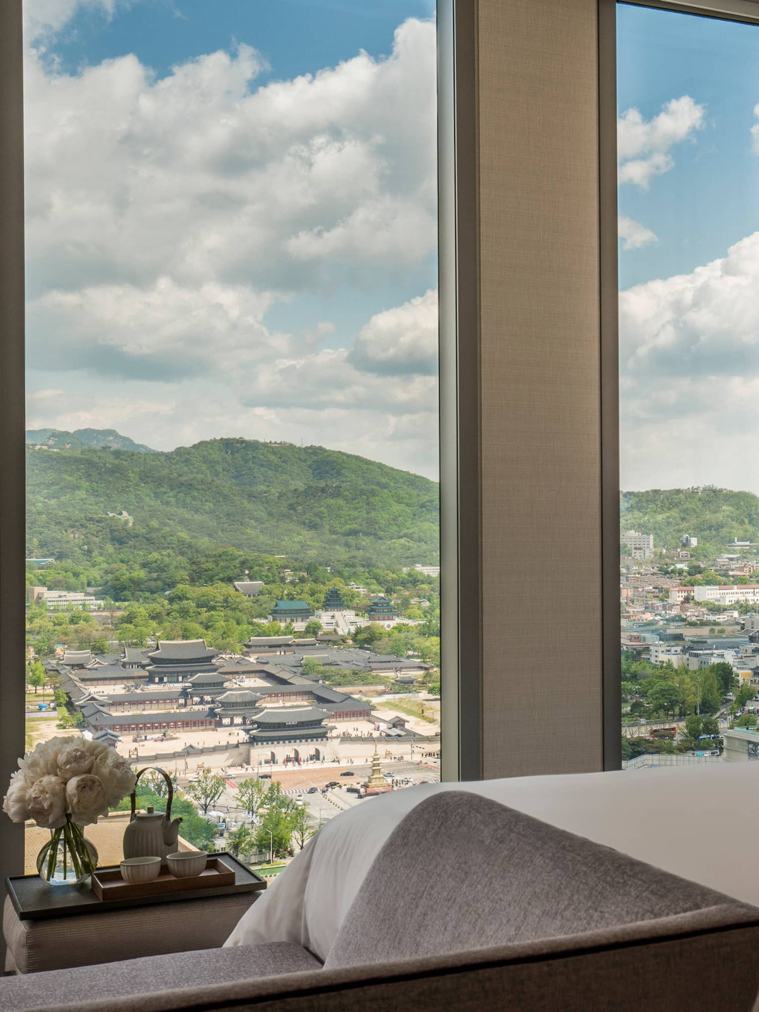 Palace-View Executive Suite bed, chaise at foot, shelf with vases, books beside window overlooking Gyeongbokgung Palace