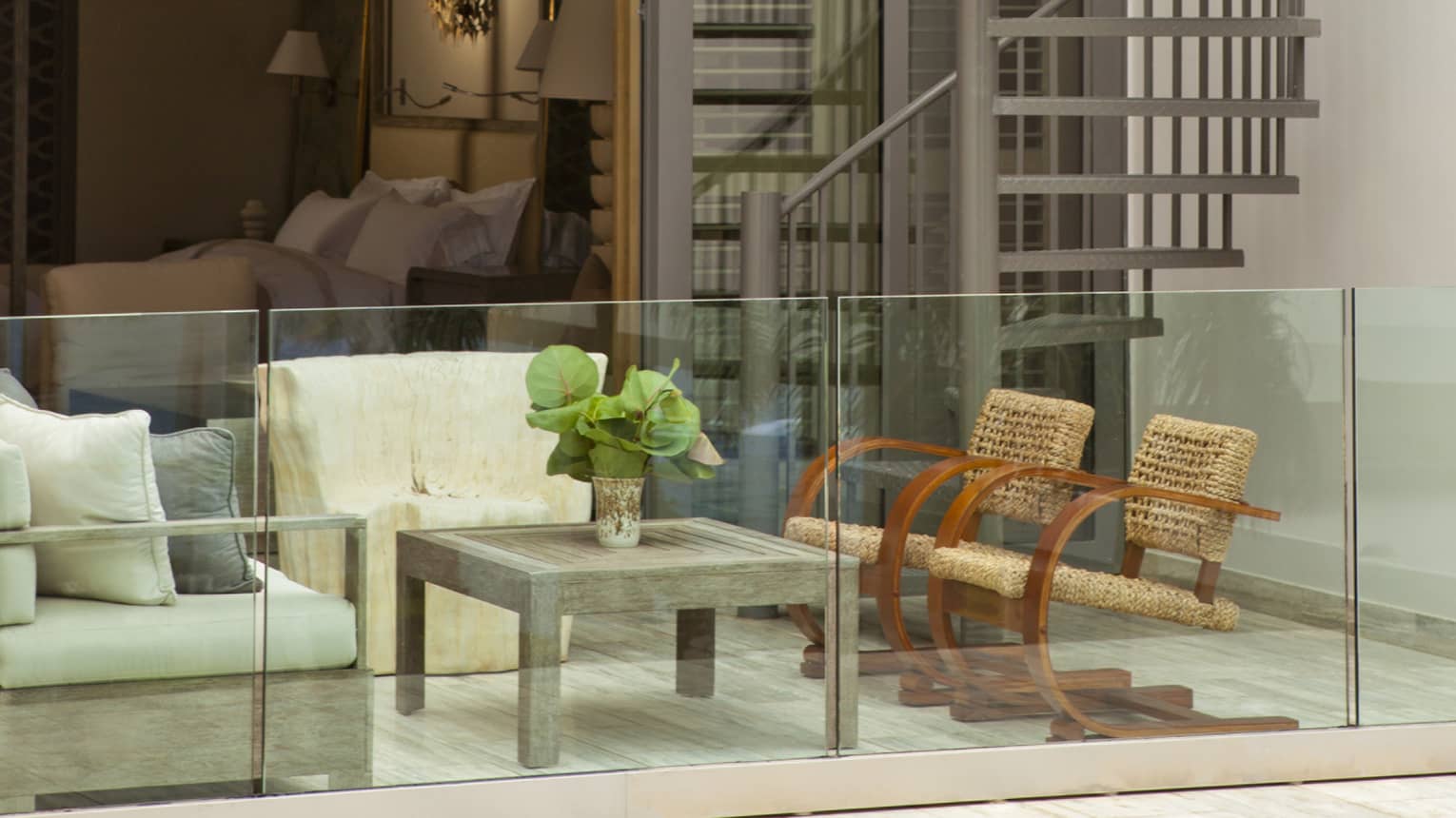 Private villa patio seating area behind glass balcony, bedroom in background, spiral outdoor staircase