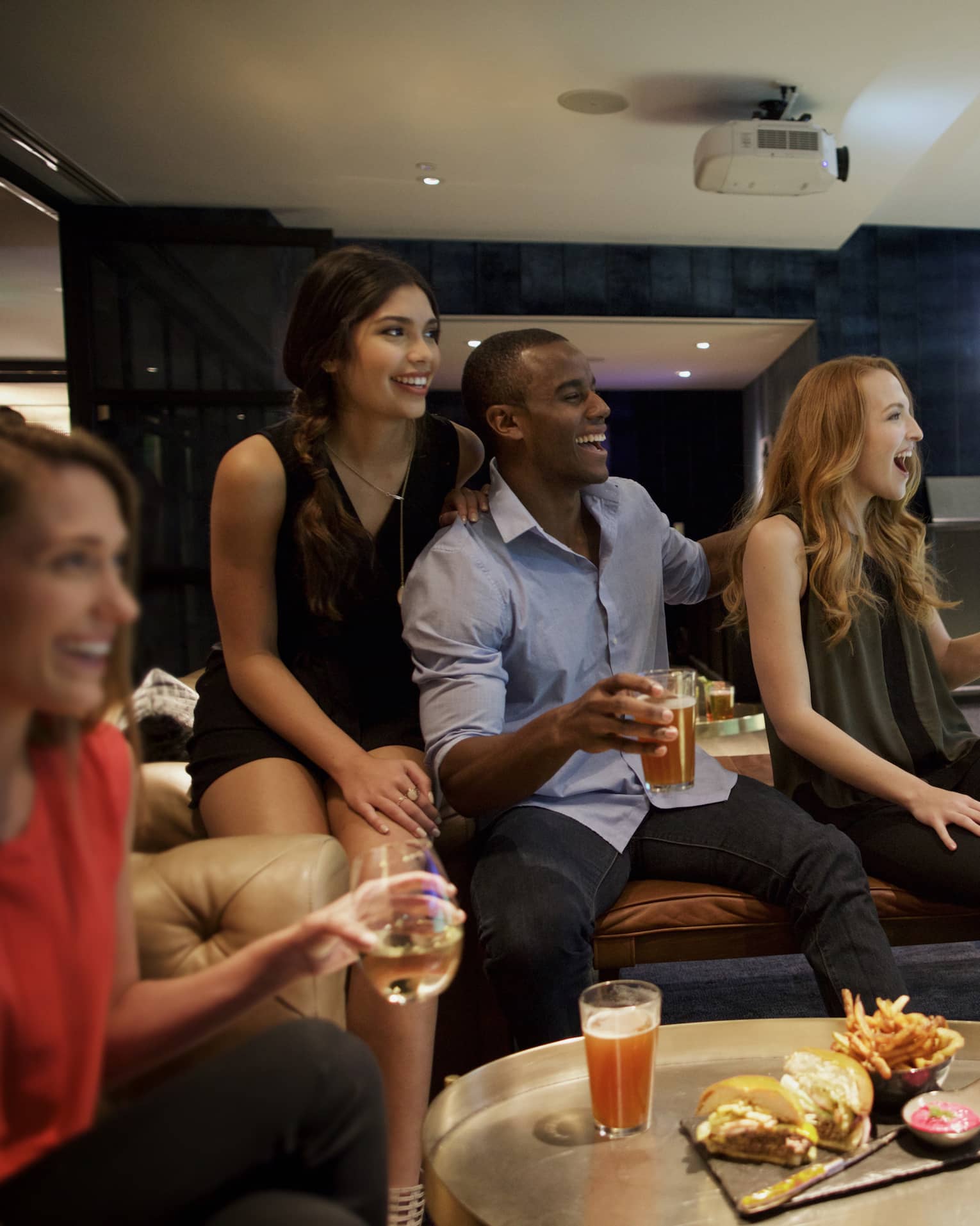A man and three woman sip beer and cheer on a sports team in the foreground, while another man golfs in the background of a function room at four seasons hotel houston