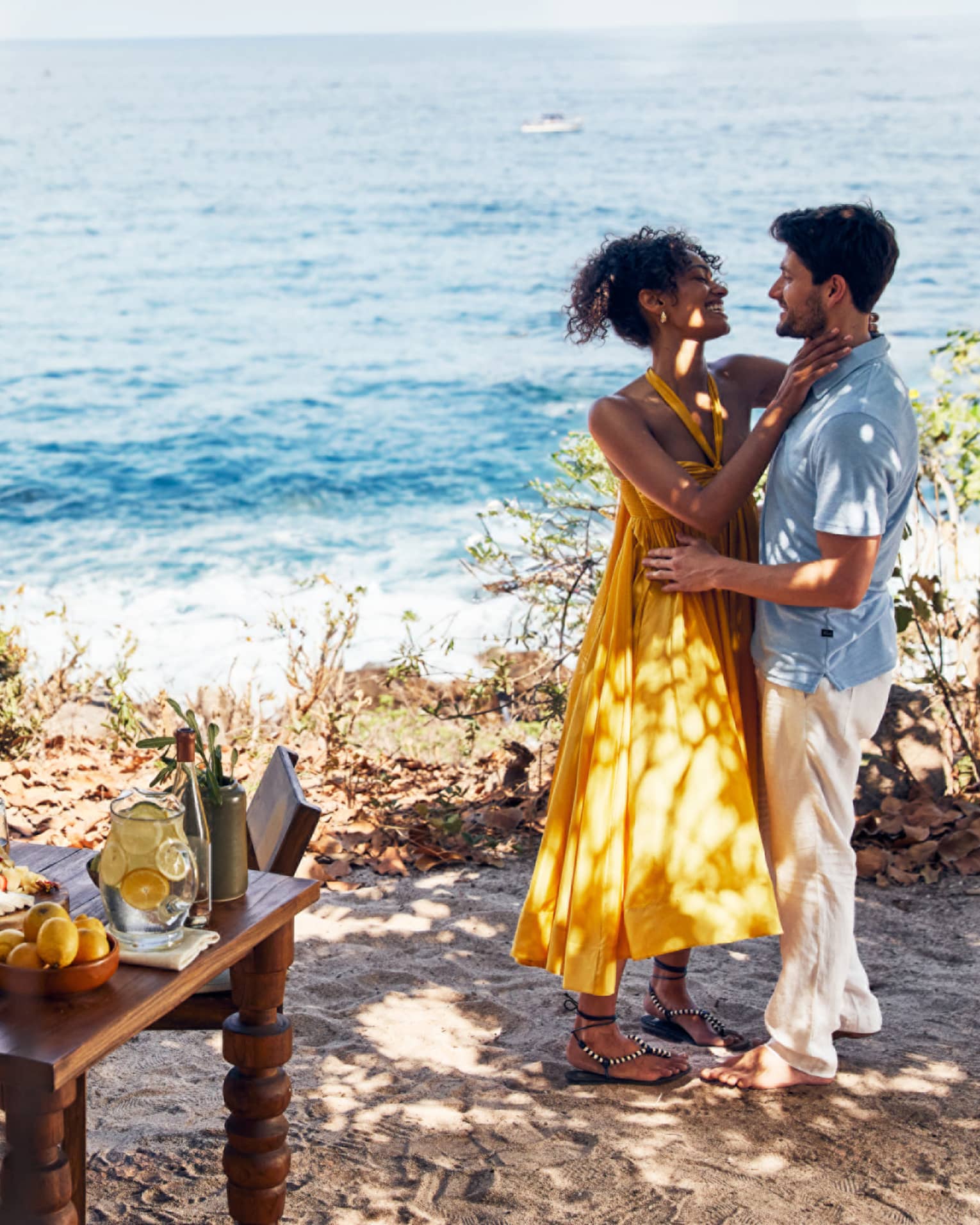 A man and woman dancing near the ocean with a small table of food near them.
