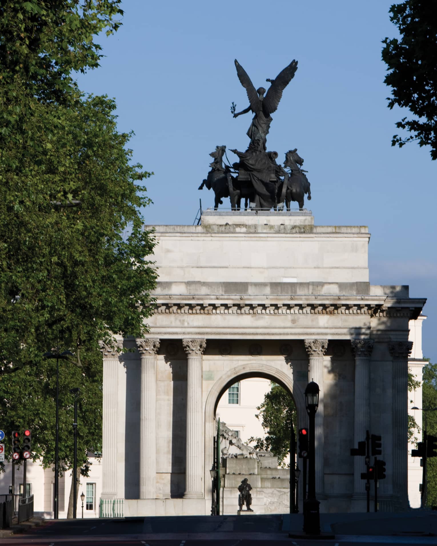 View through trees to Wellington Arch monument and statue against blue sky
