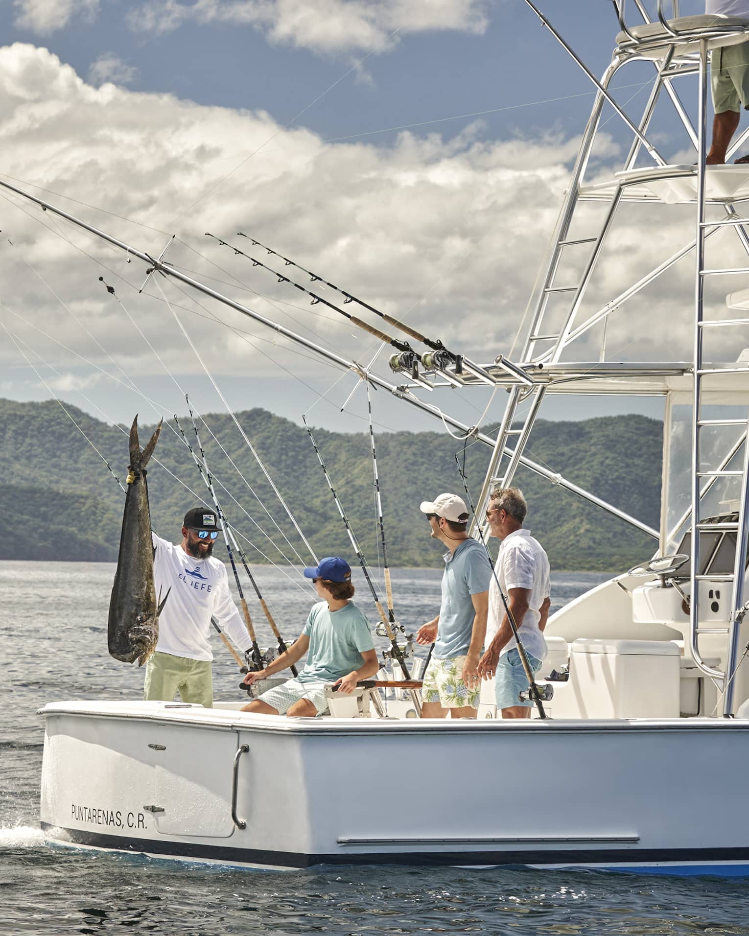 Four men are gathered on the back of a fishing boat with one of them holding a large fish up by the tail