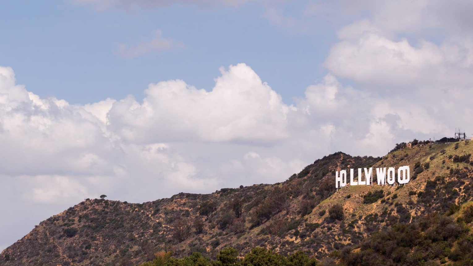 Hollywood sign on green Los Angeles hills against blue sky