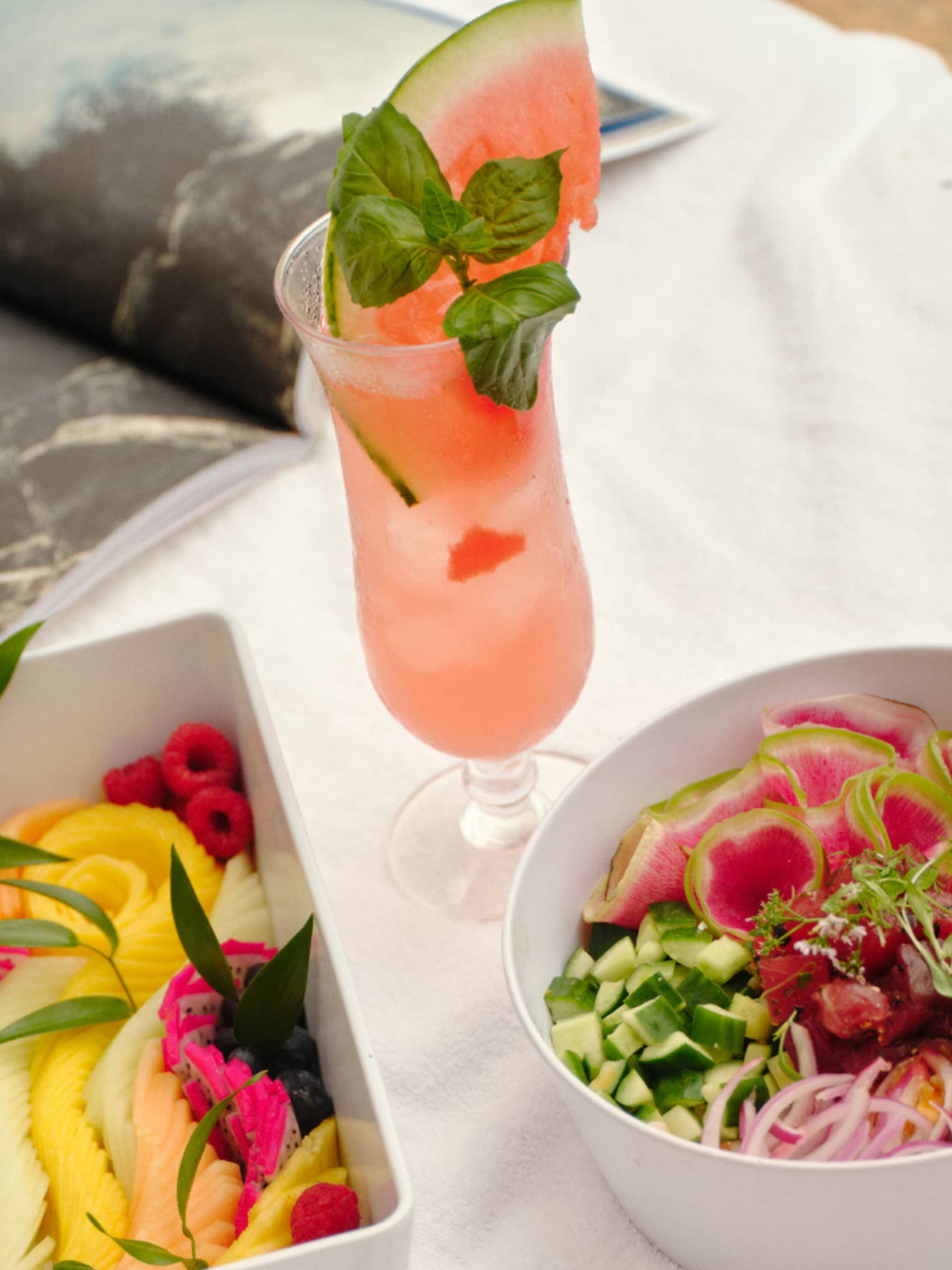 Fresh fruit and salad in white containers set on a day bed