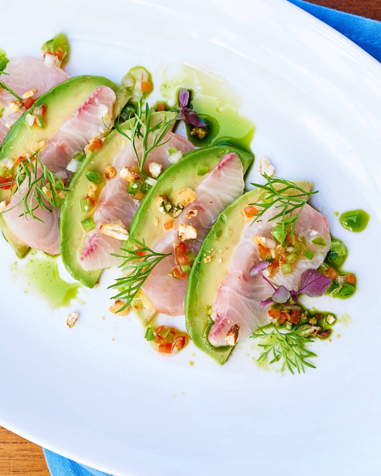 Kanpachi Crudo sliced fish arranged with avocado, toasted corn, greens