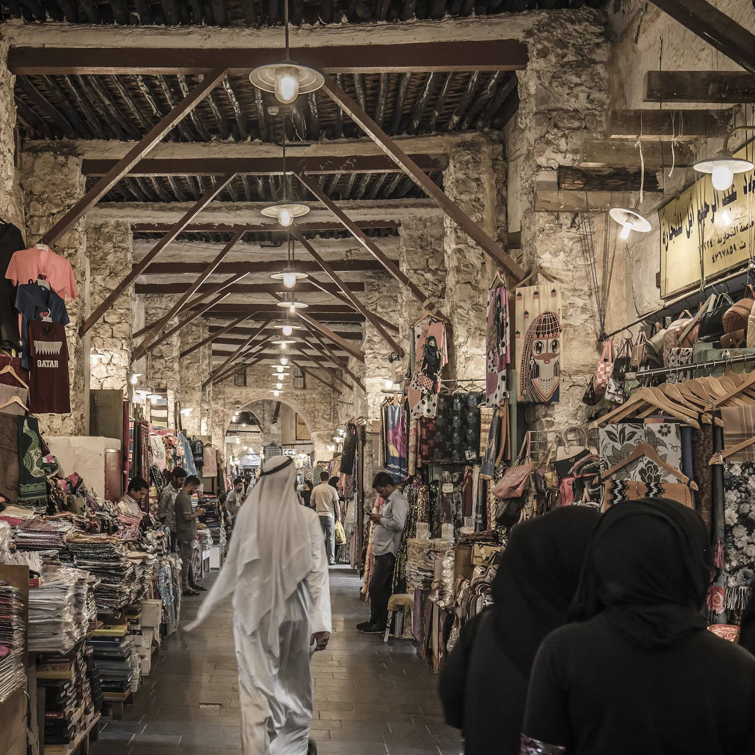 People walk past tables with textiles, clothes in indoor market