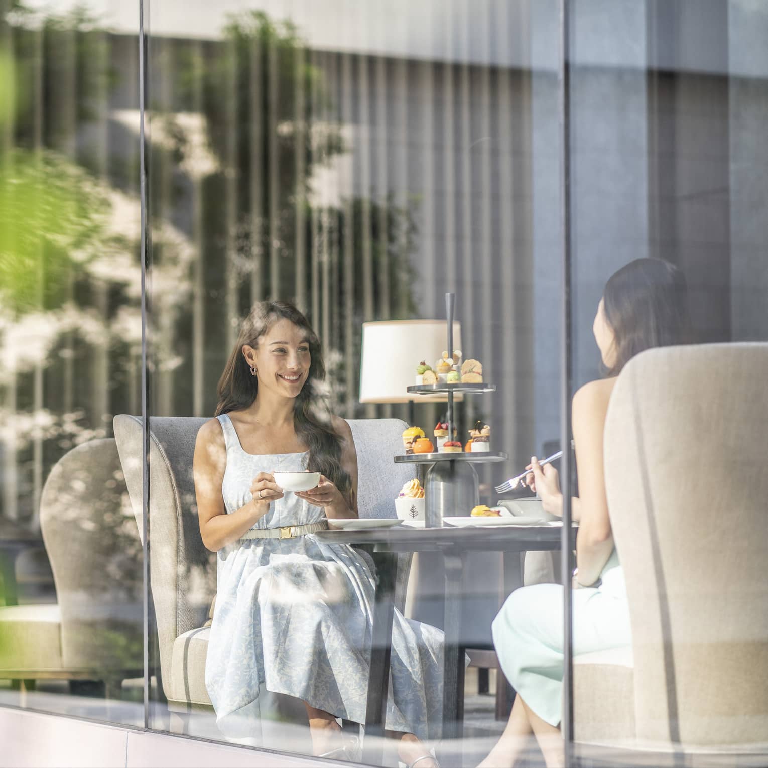 View through cafe glass window where two women enjoy afternoon tea and desserts