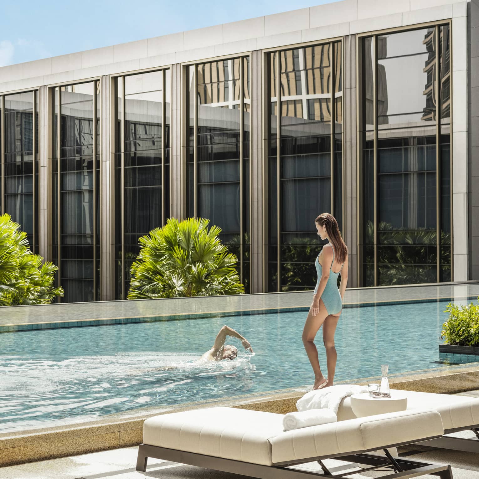 Man swims laps as woman in blue bathing suit watches poolside