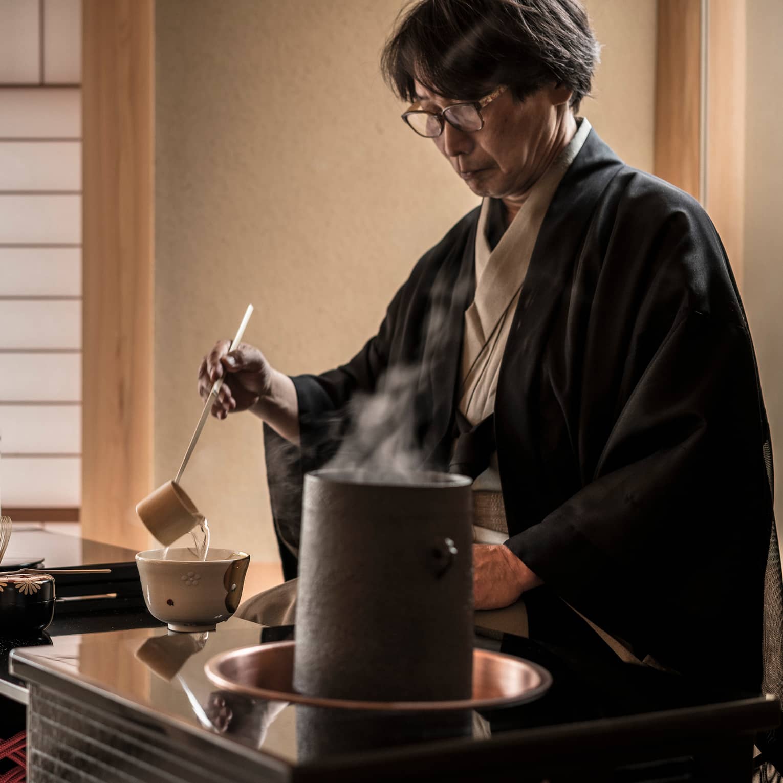 Man ladles hot tea into cup on table in teahouse by steaming pot