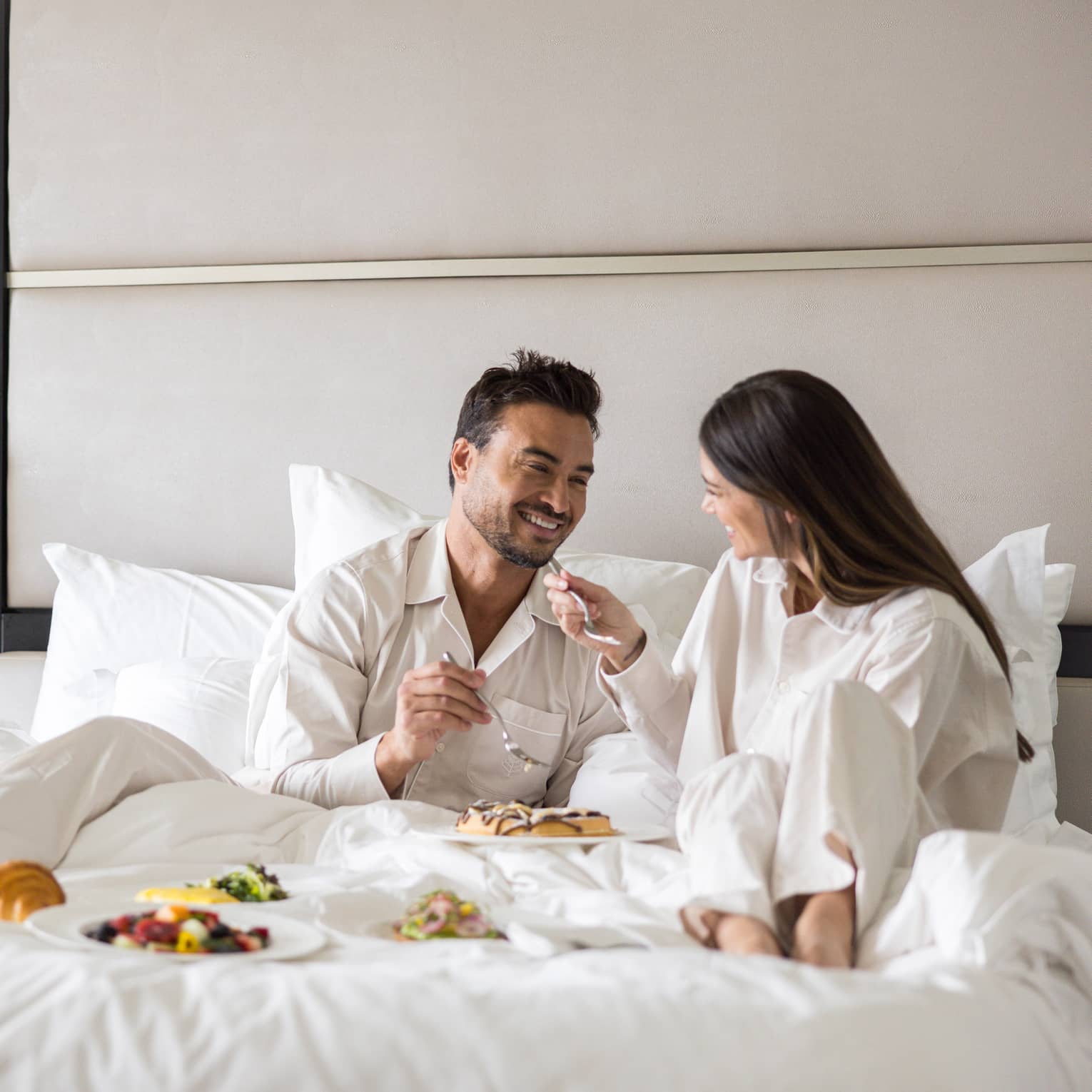 Man and woman eat breakfast in bed in luxury hotel room