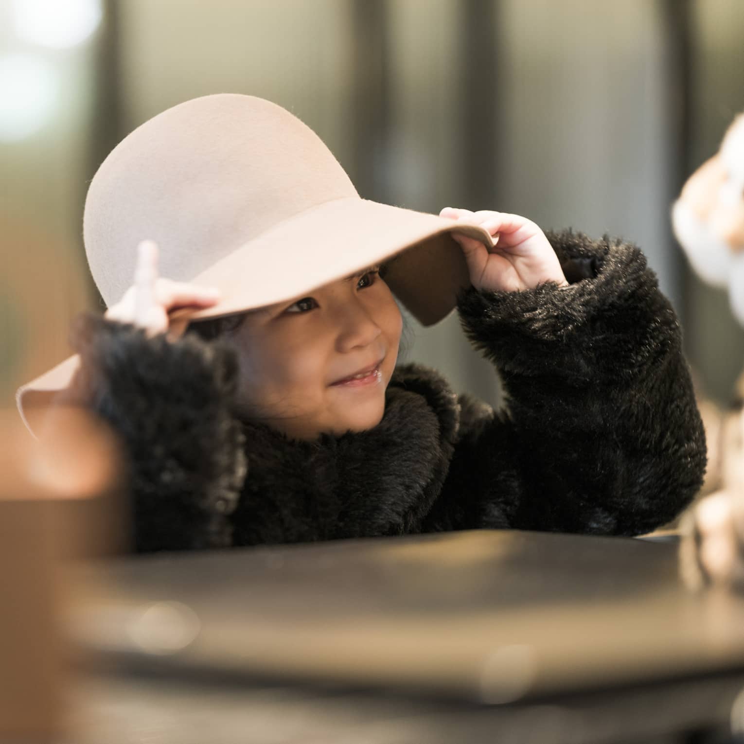 Smiling young girl in wide-brim pink hat and faux fur coat