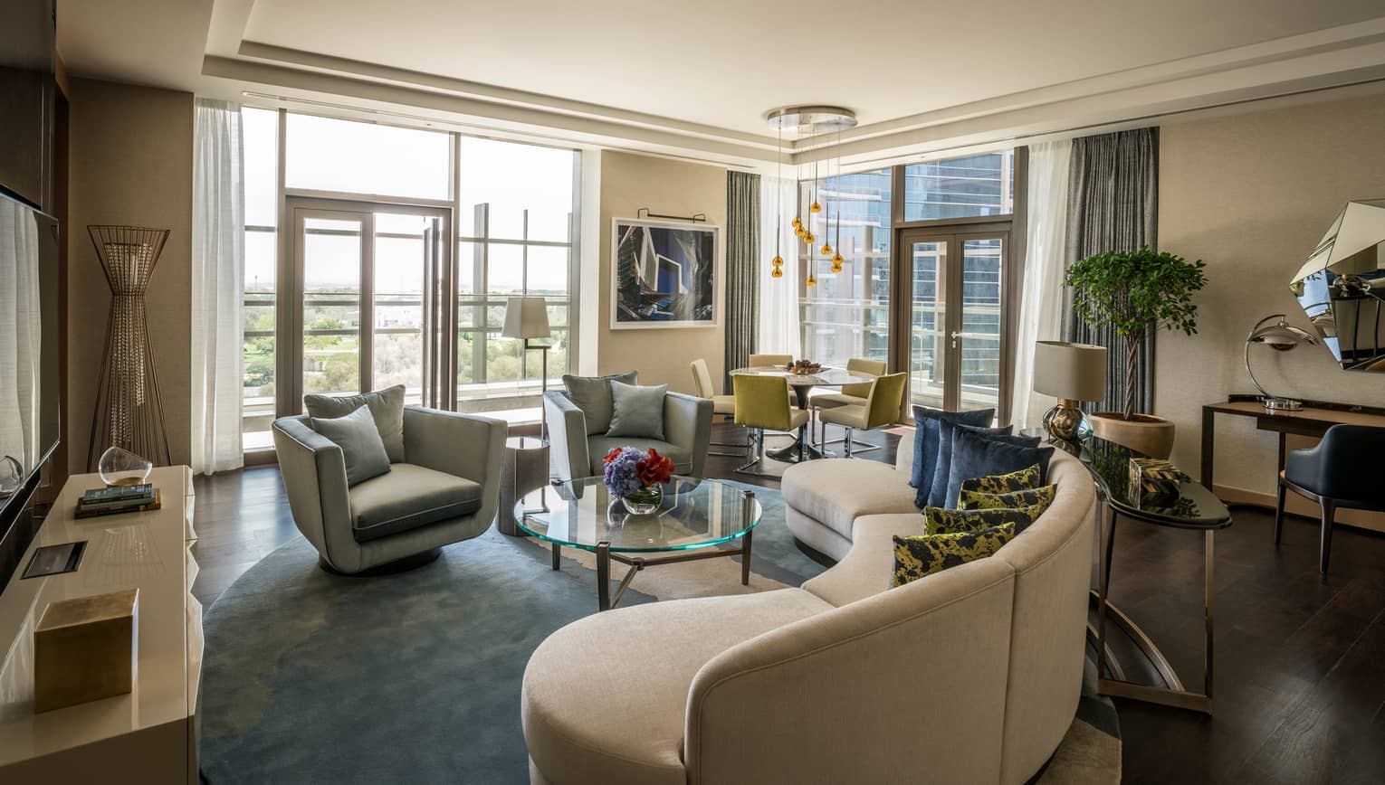 Residential Suite living room with large curved beige sofa, plush armchairs, corner windows, modern lamps