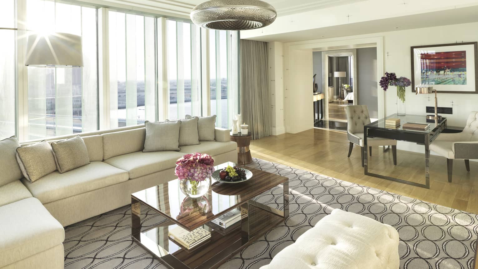 Deluxe Four Seasons Executive Suite living room with L-shaped white sofa, bench against bright window, dining table