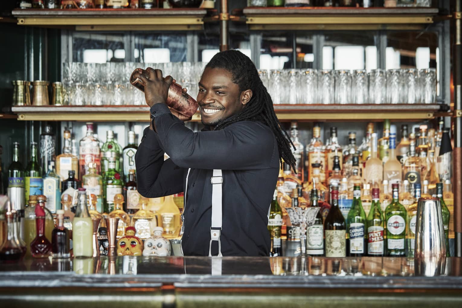 Smiling Butcher & Still bartender shakes cocktail behind bar, liquor display