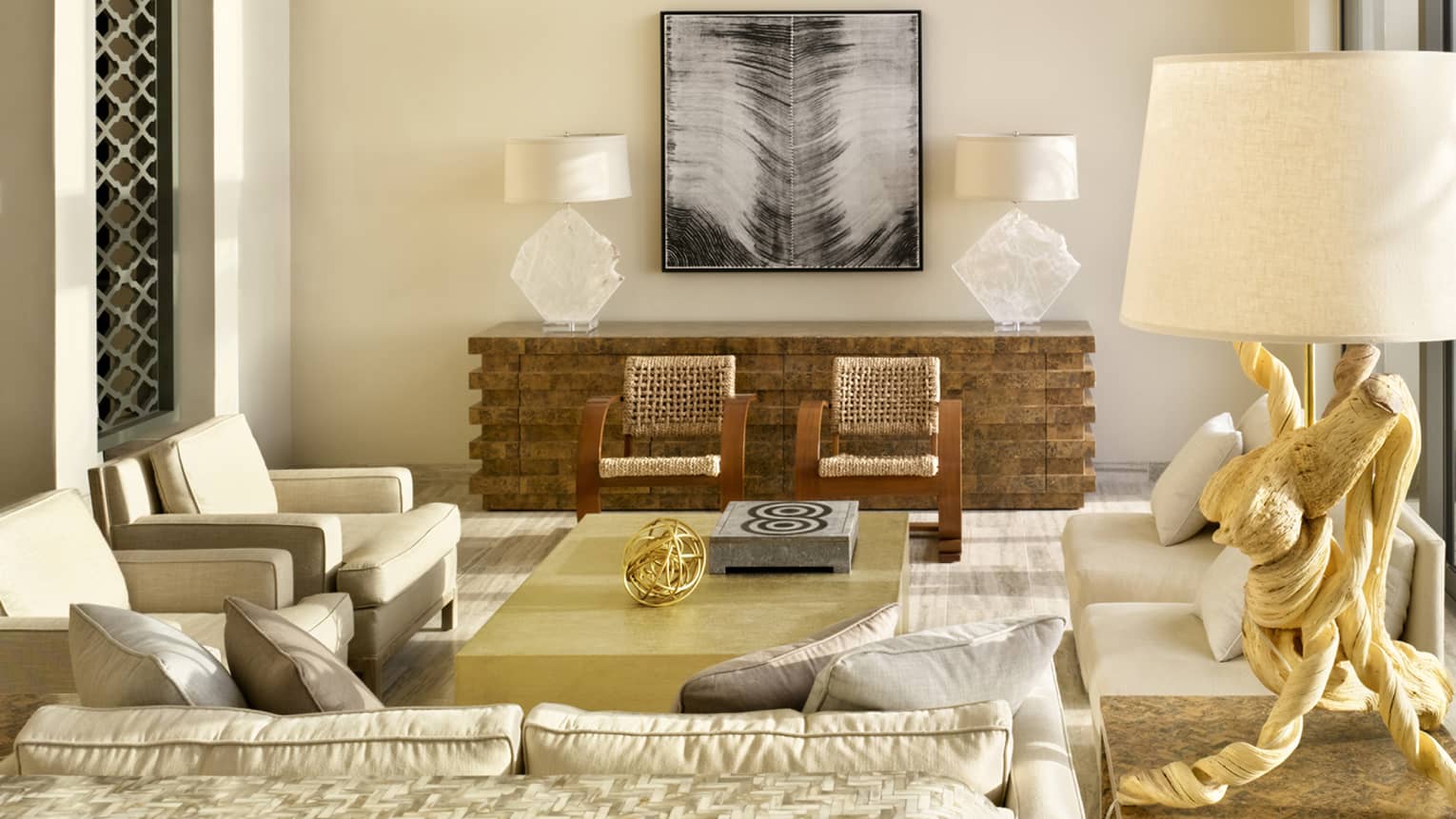 Stylish living room with beige sofa and armchairs, woven chairs, a gold coffee table, decorative lamps and abstract wall art